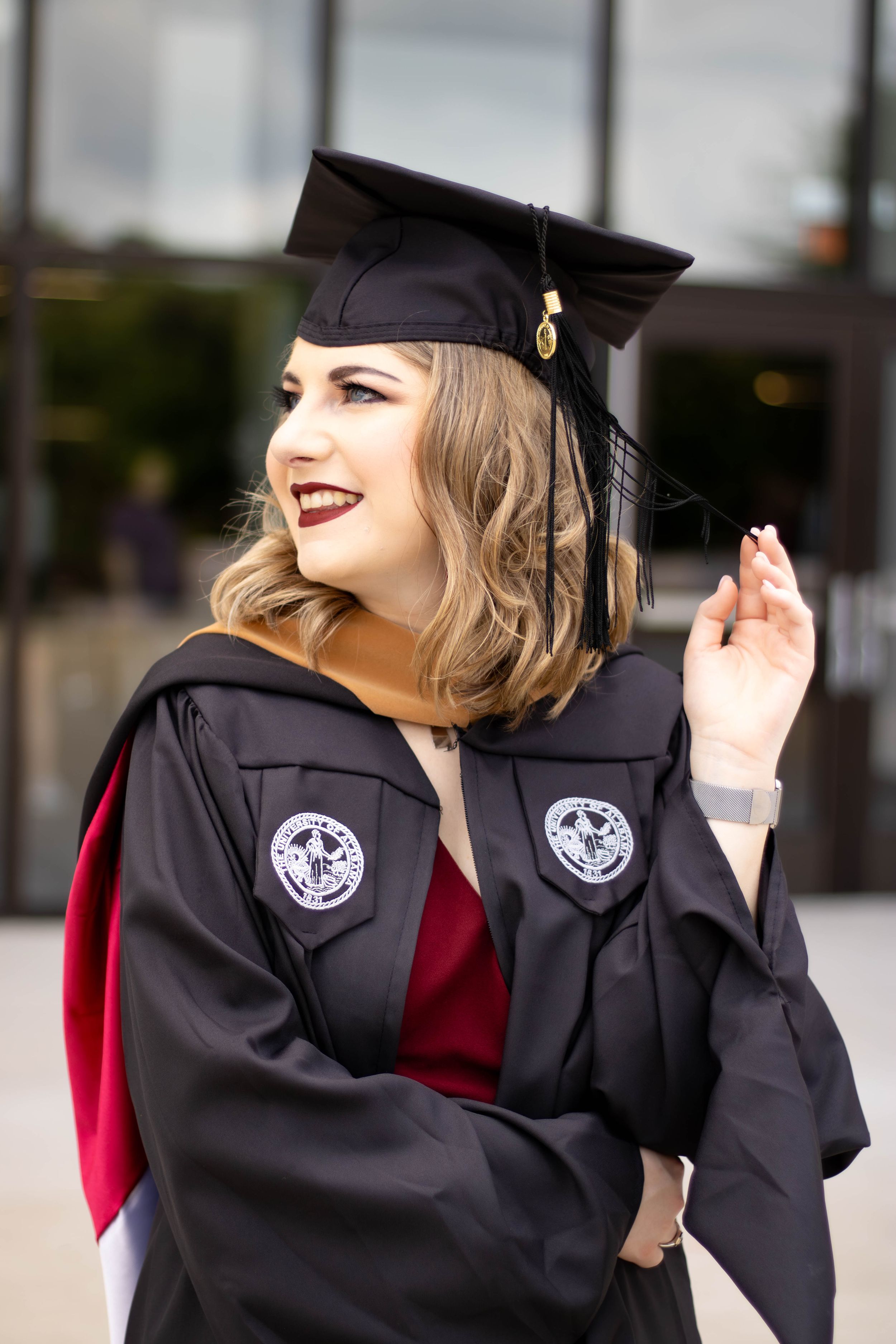 Graduate in black cap and gown with red trim smiling during graduation celebration.