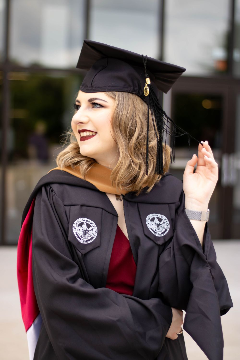 Graduate in black cap and gown with red trim smiling during graduation celebration.