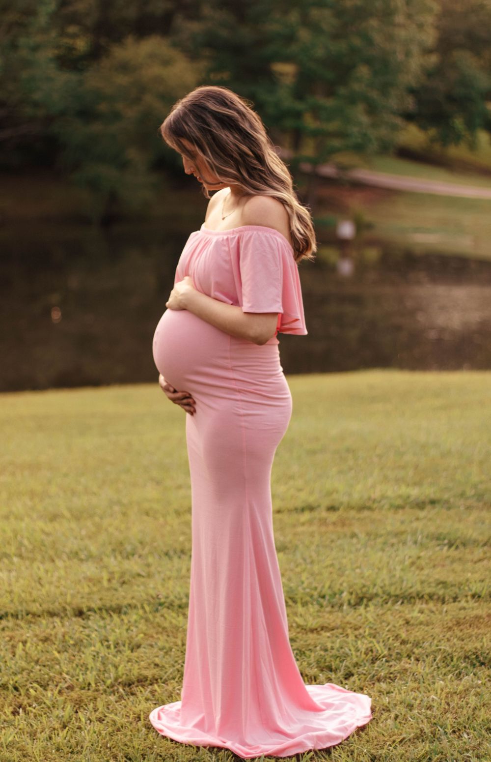 Maternity photo of woman in flowing pink dress standing in grassy field.