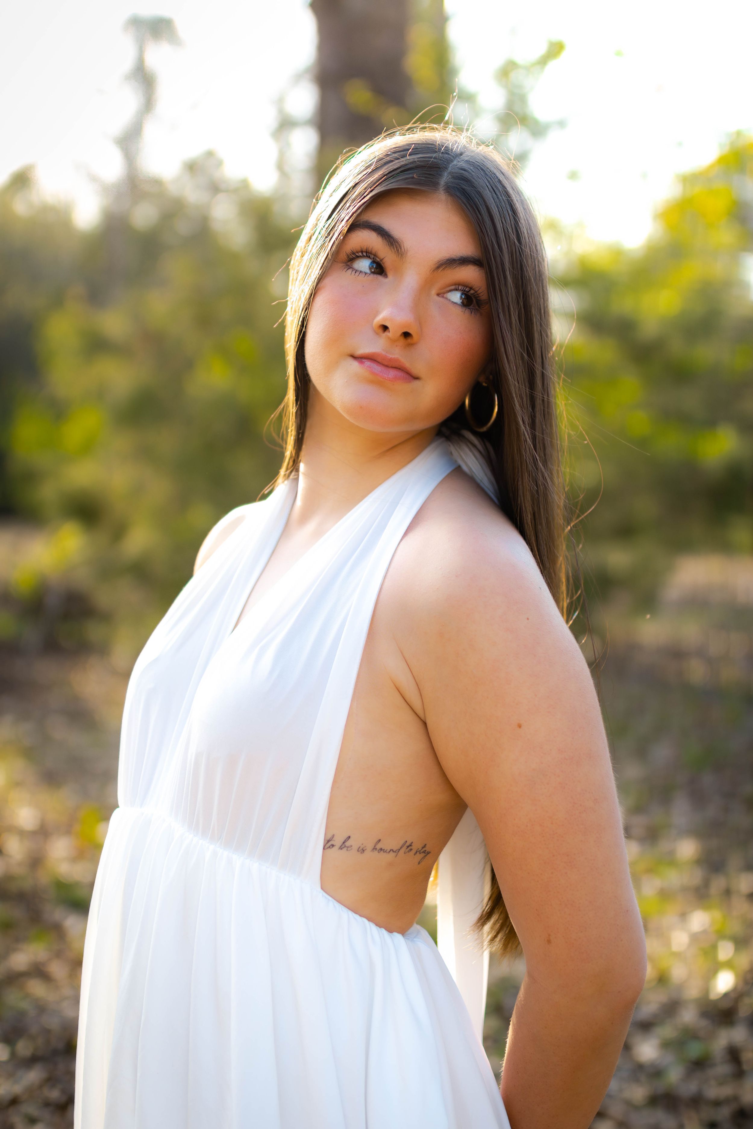 Person in flowing white dress poses in golden sunset light.