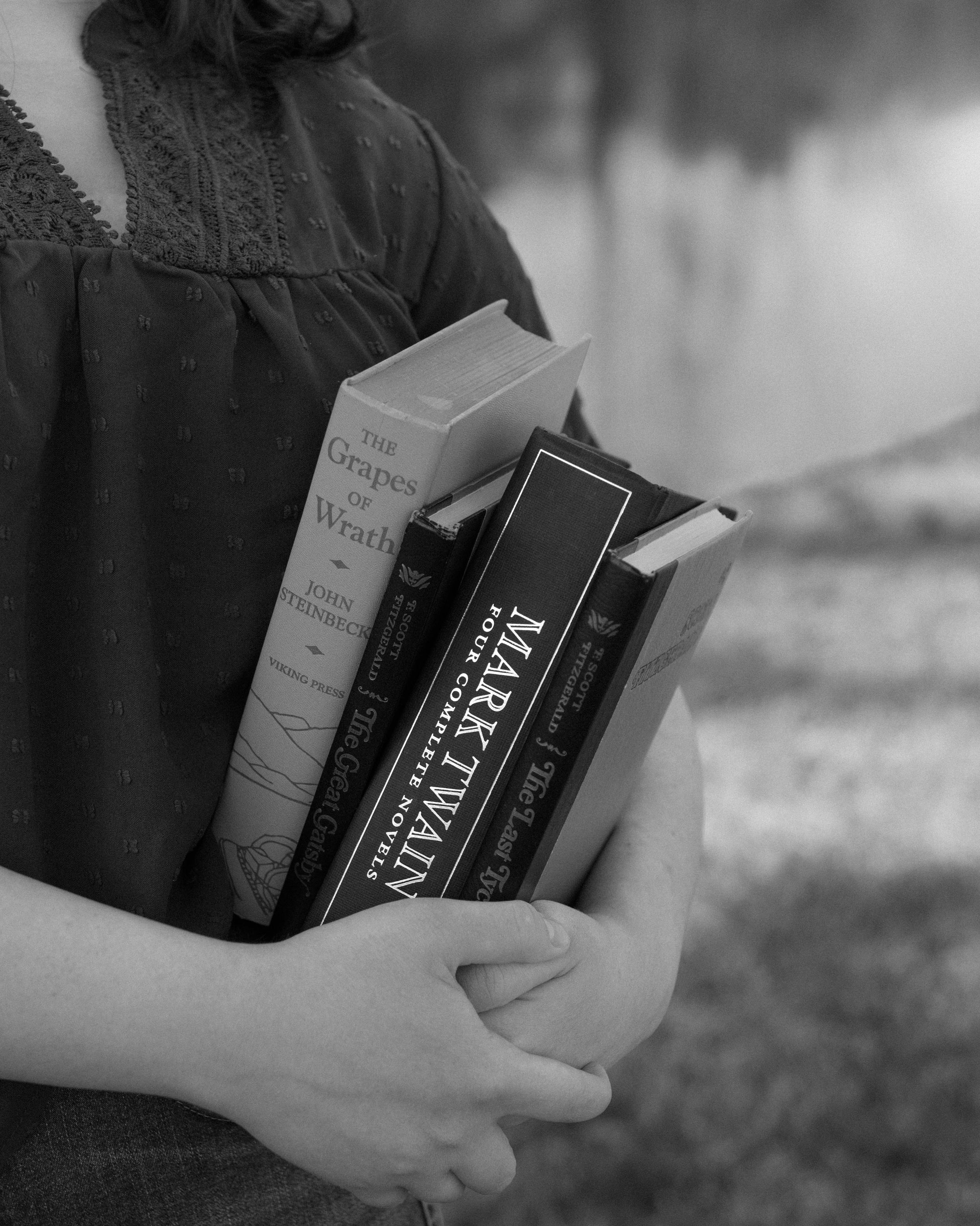 Black and white photo of hands holding several vintage hardcover books.