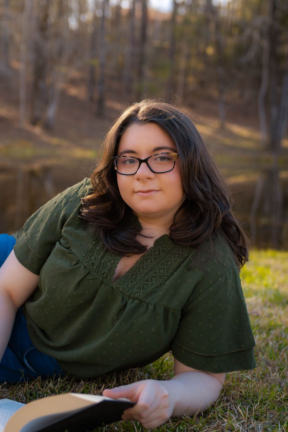 Graduate in green dress relaxing outdoors by a pond.