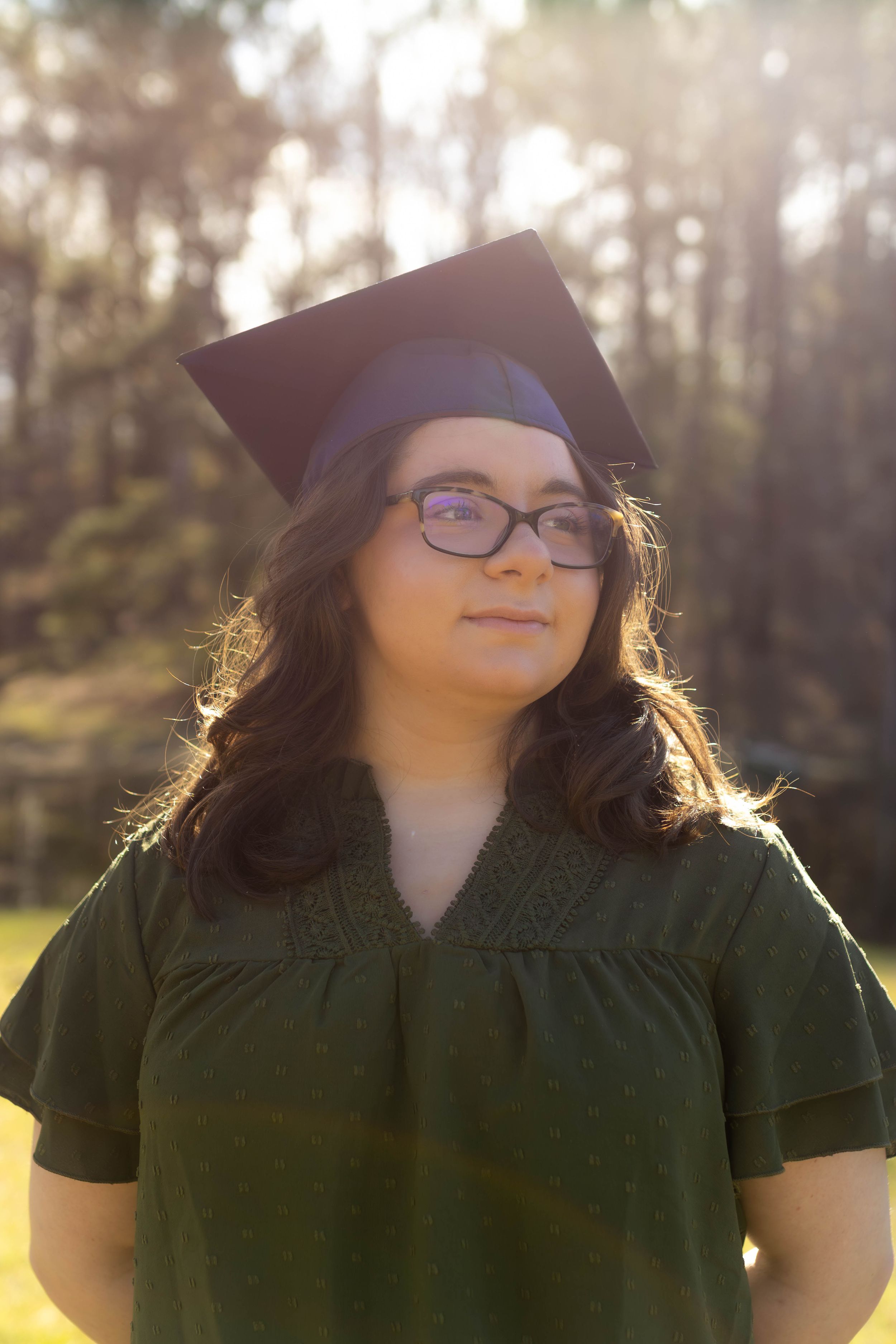 Graduation portrait with backlit trees and sunlight creating a warm glow.