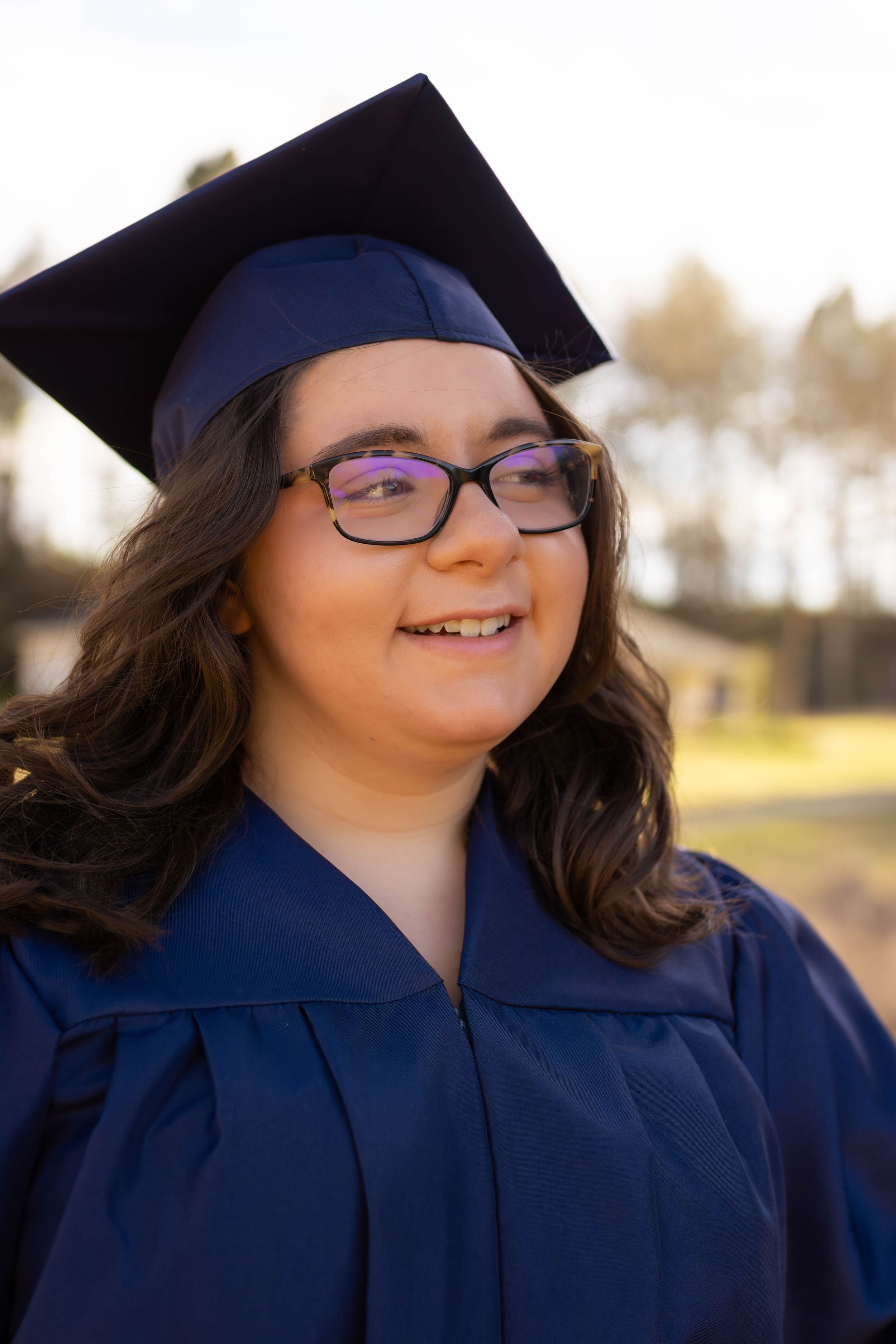 Graduate wearing blue cap and gown smiling outdoors.