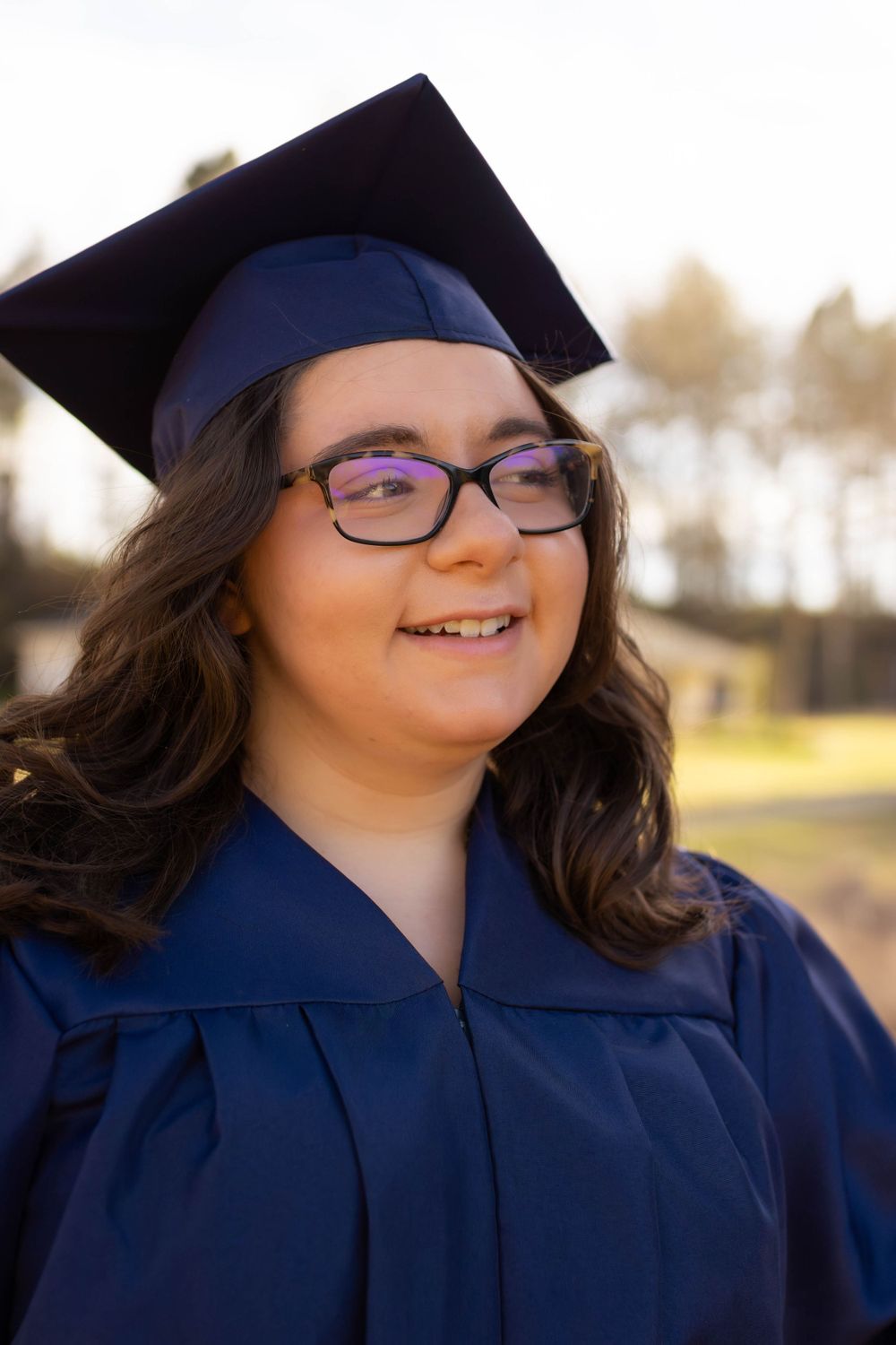 Graduate wearing blue cap and gown smiling outdoors.