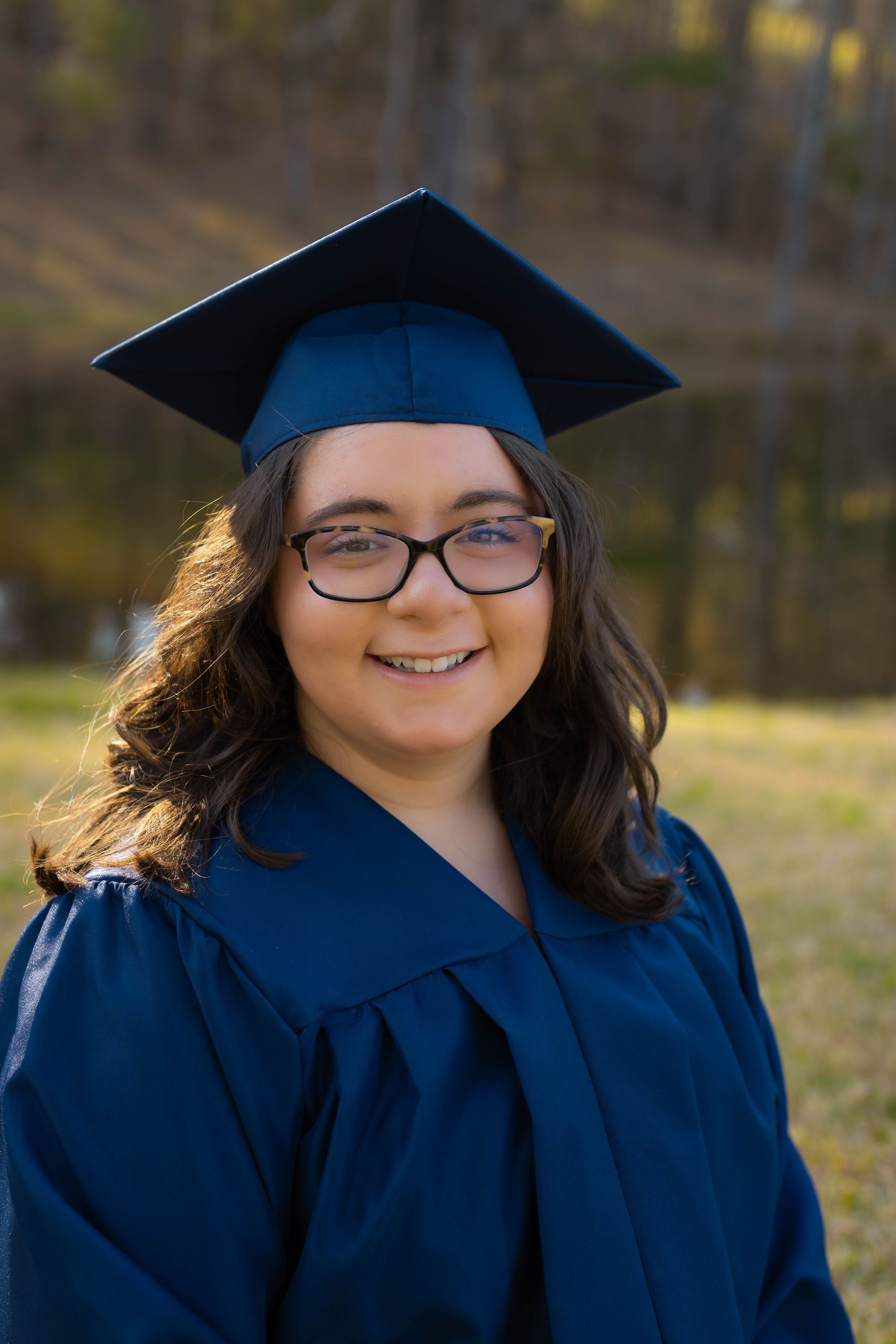 Graduate in traditional blue cap and gown smiling outdoors.