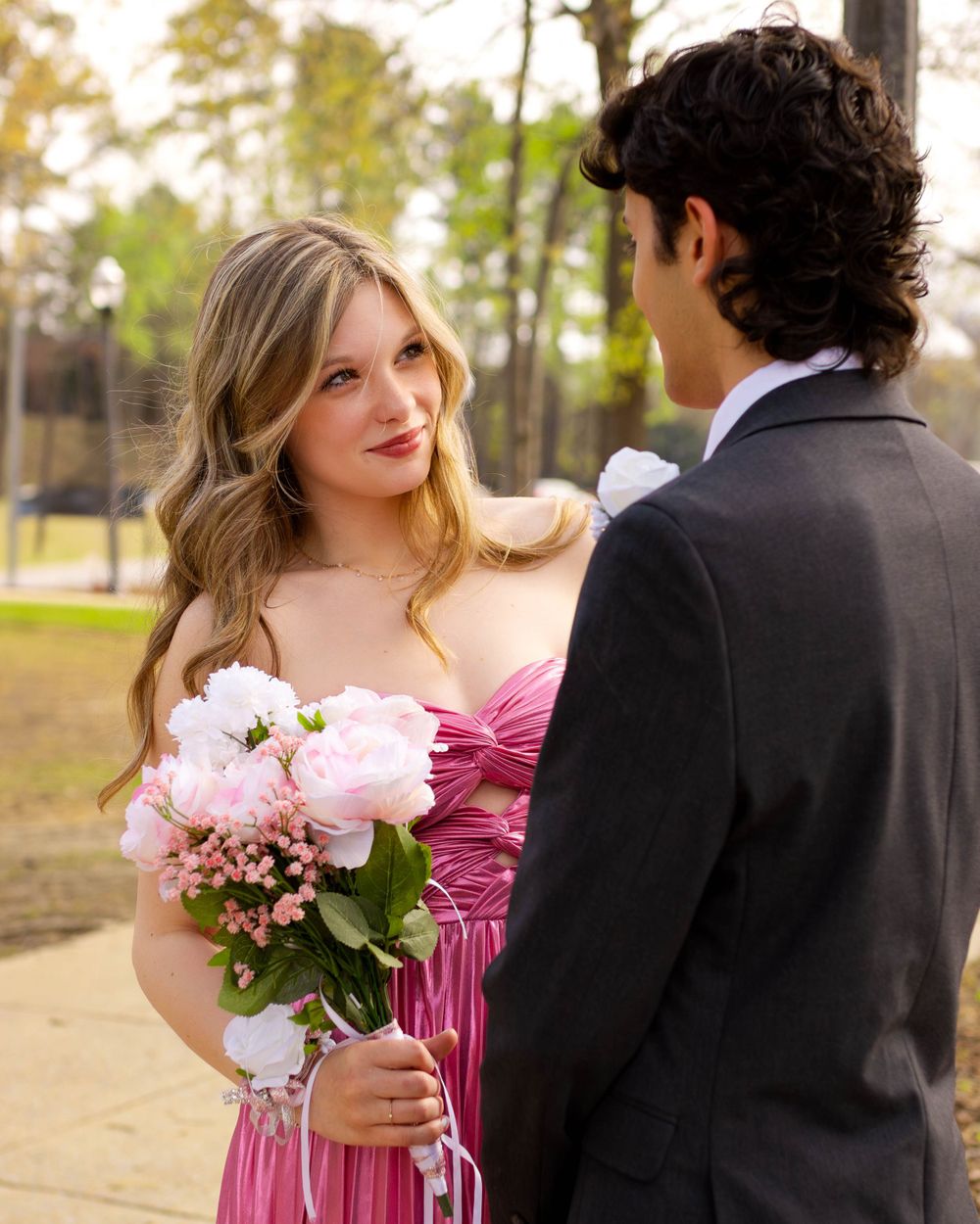 Formal couple in pink attire share a romantic moment during prom photos.