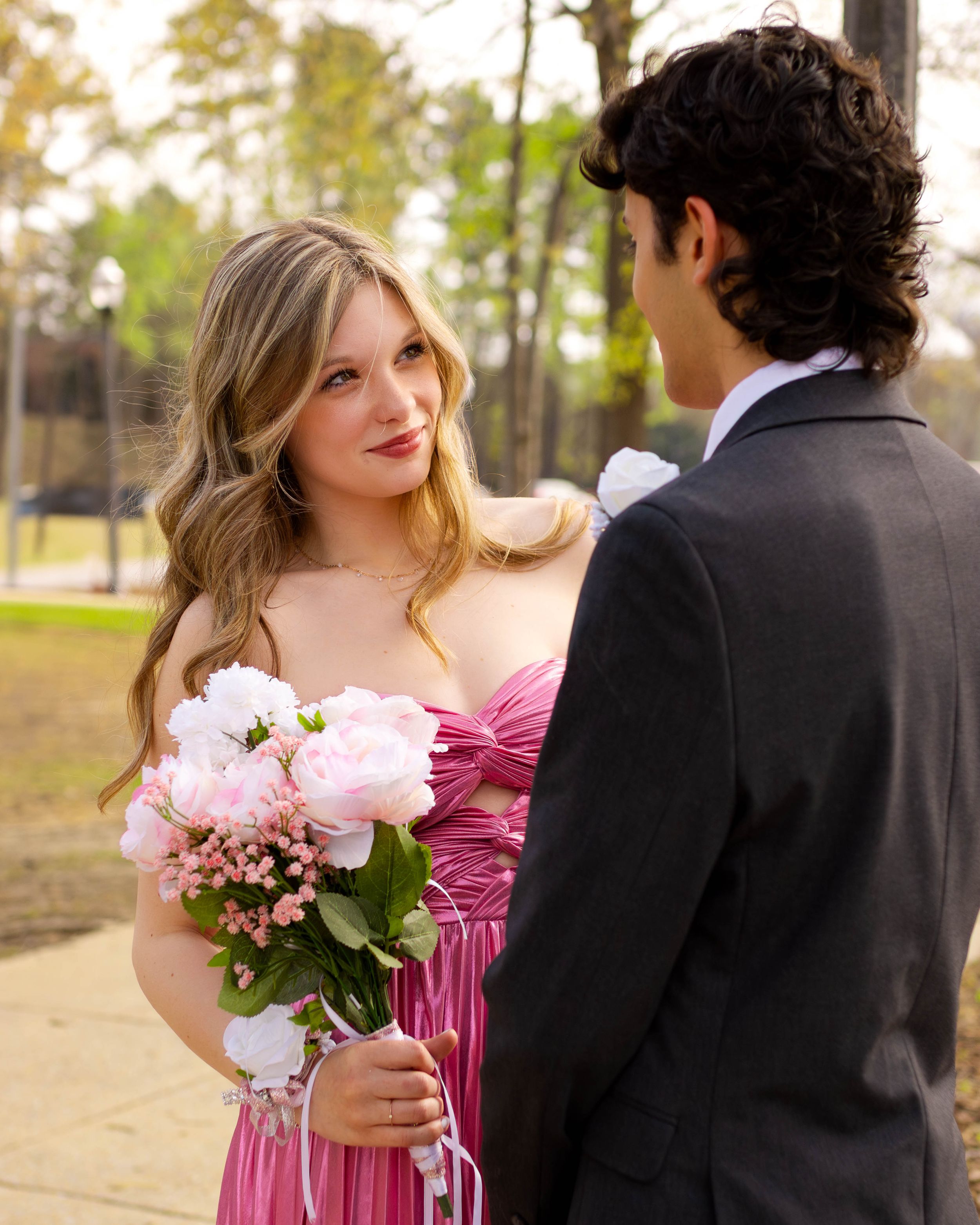 Formal couple in pink attire share a romantic moment during prom photos.