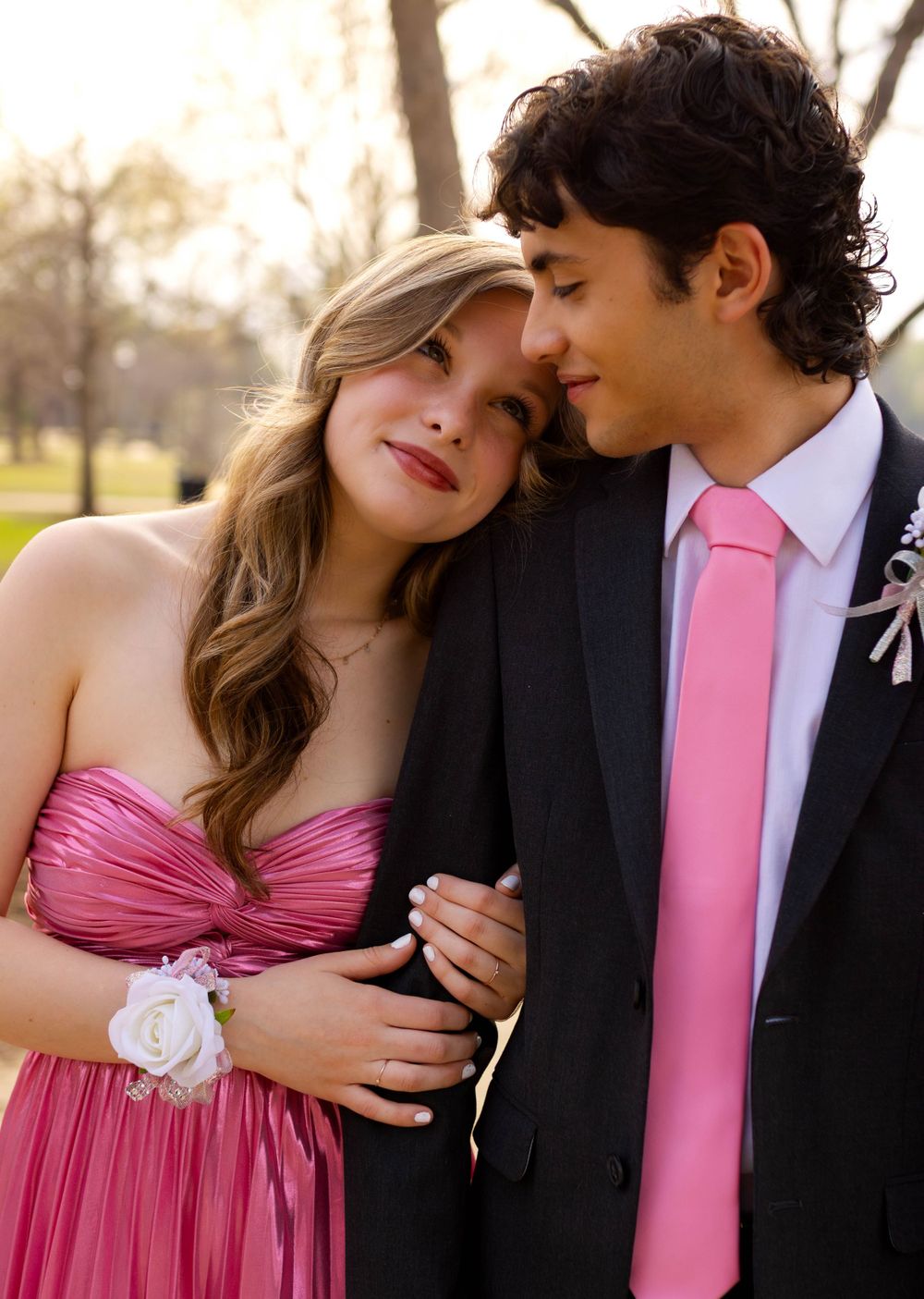 A romantic prom couple in coordinating pink attire share an intimate moment outdoors.