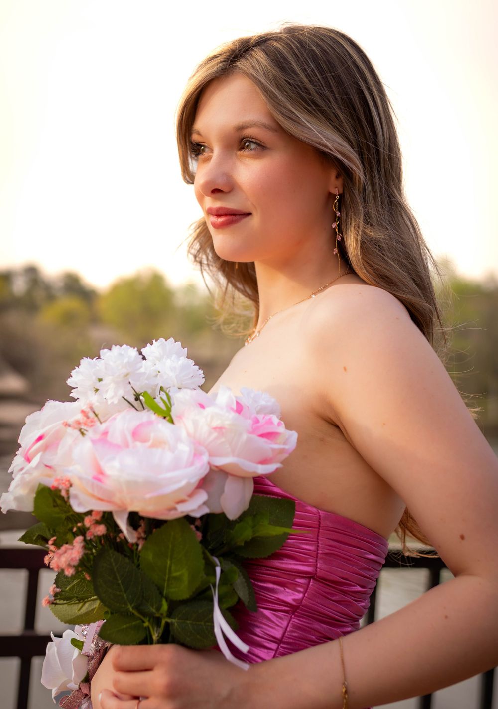 Elegant prom attendee in a pink strapless dress holds a bouquet of pink and white flowers.