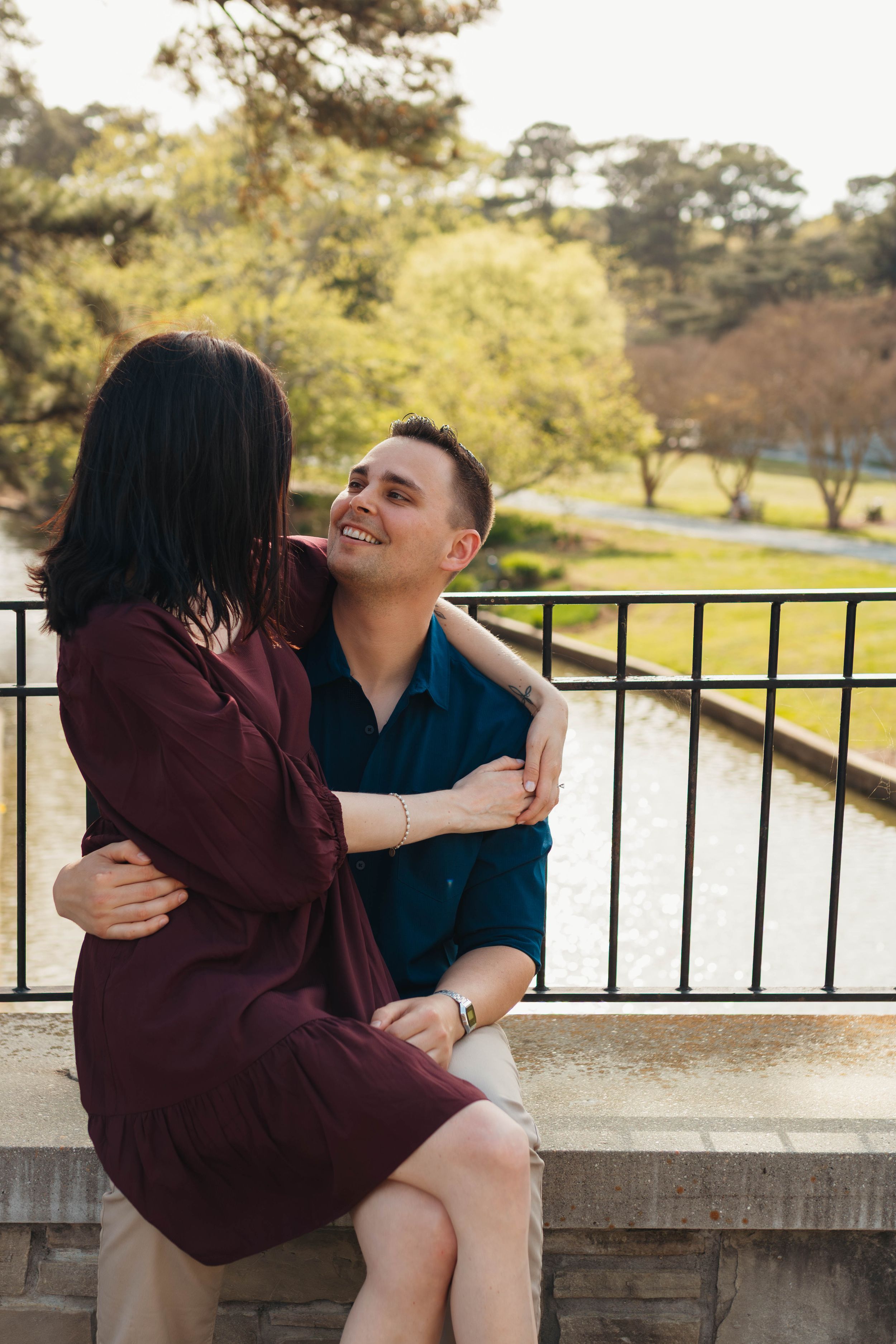 Couple embraces on stone ledge during romantic outdoor photoshoot.