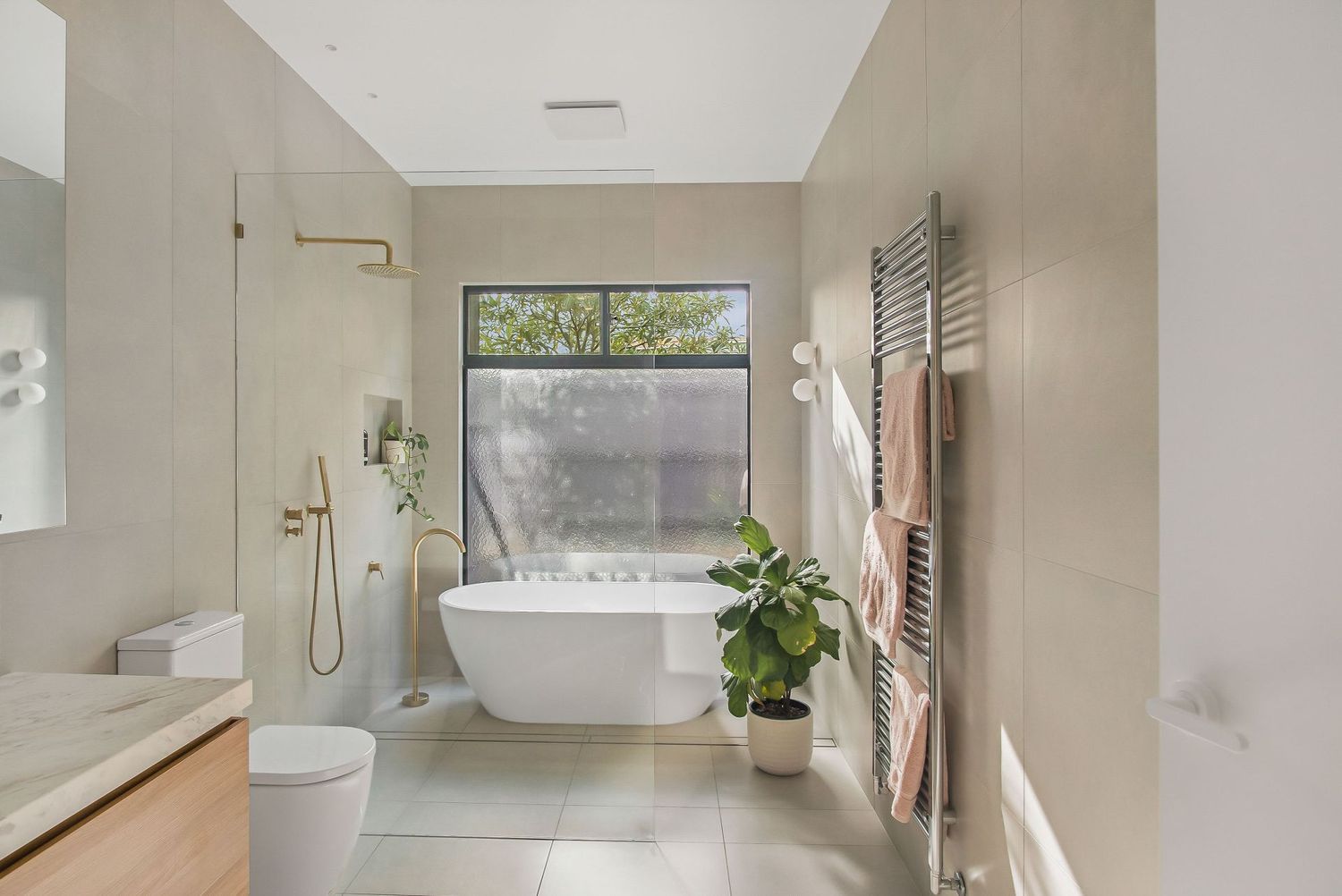 Bright bathroom featuring freestanding tub, window, and heated towel rail with natural decor.