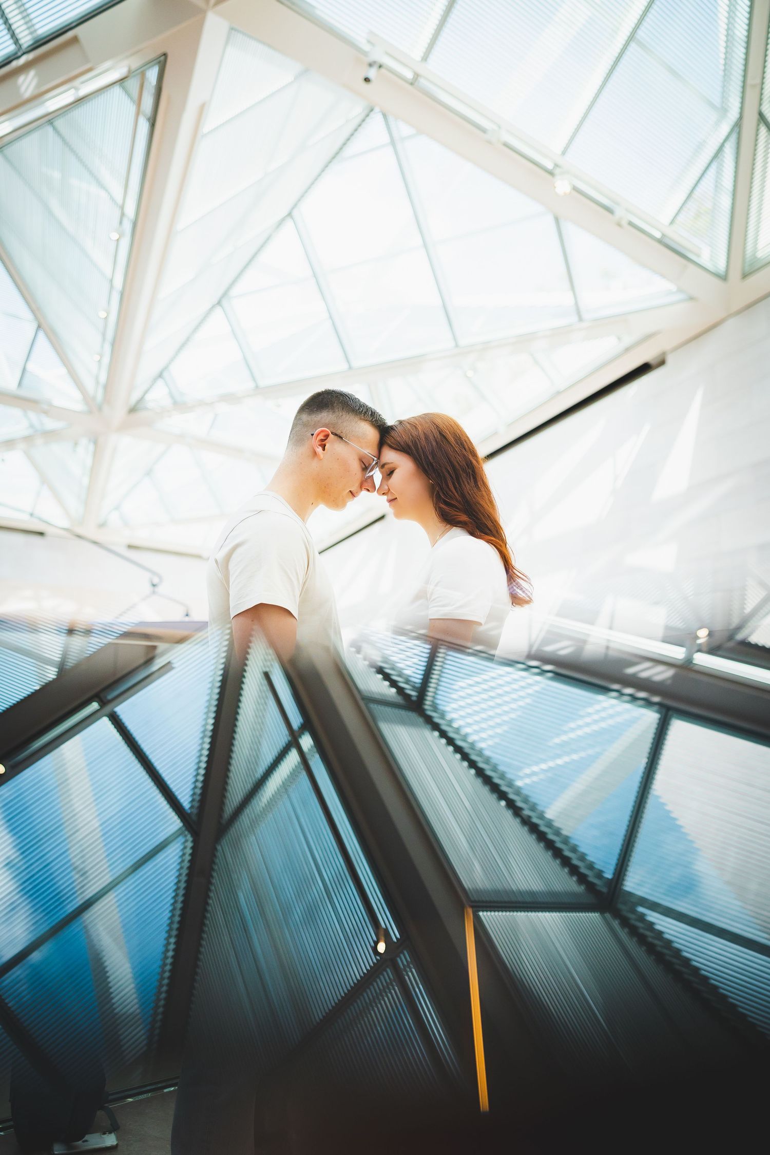 A couple stands against a modern glass ceiling with dramatic architectural angles at the National Gallery of Art East Wing