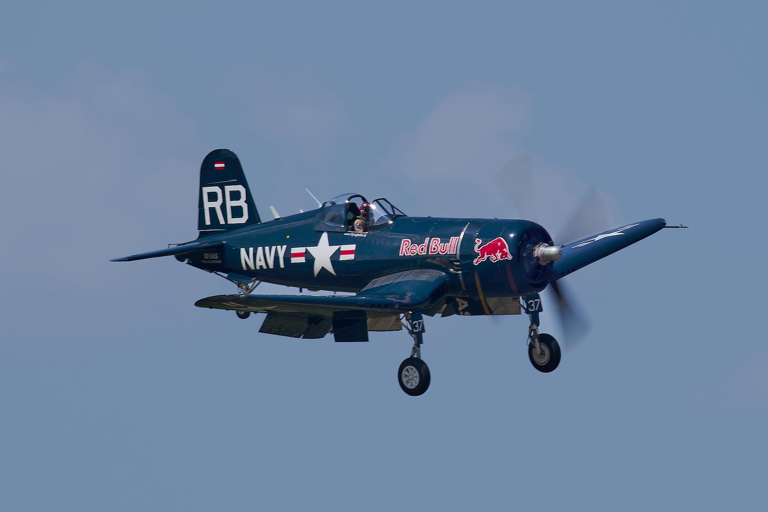 Vintage Navy aircraft with RB markings flies against blue sky during airshow demonstration.