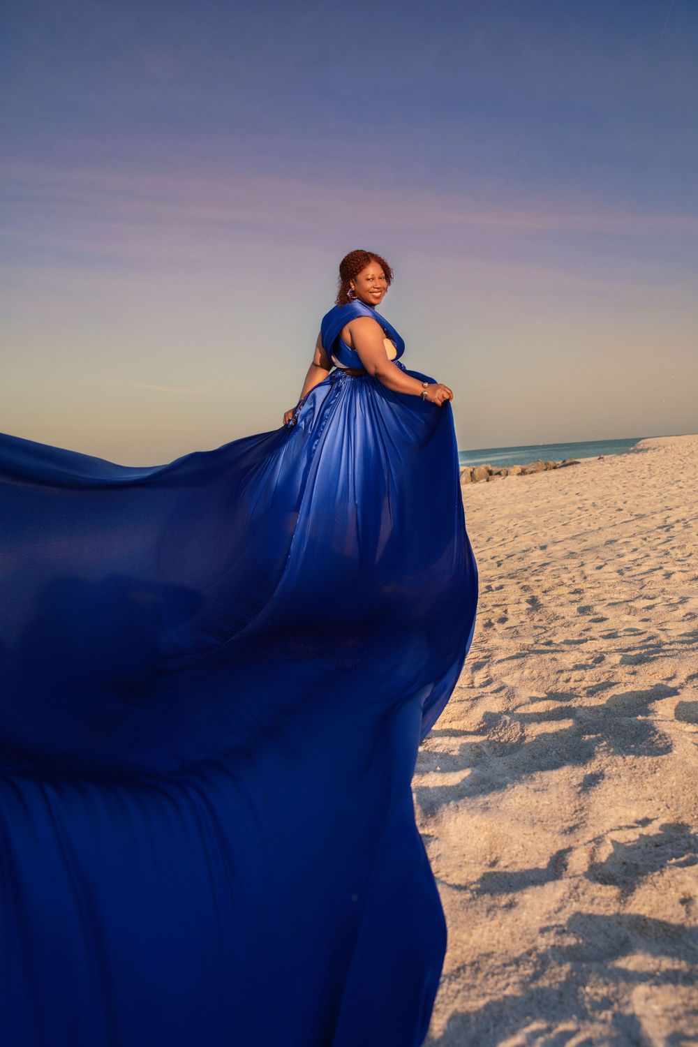 Flowing blue dress fabric photographed against white sandy beach at dusk.