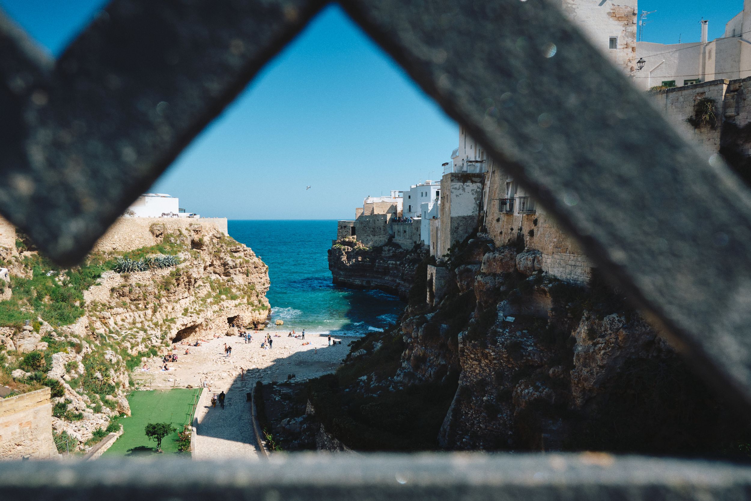 Dramatic coastal view through metal railings of a beach nestled between rocky cliffs.