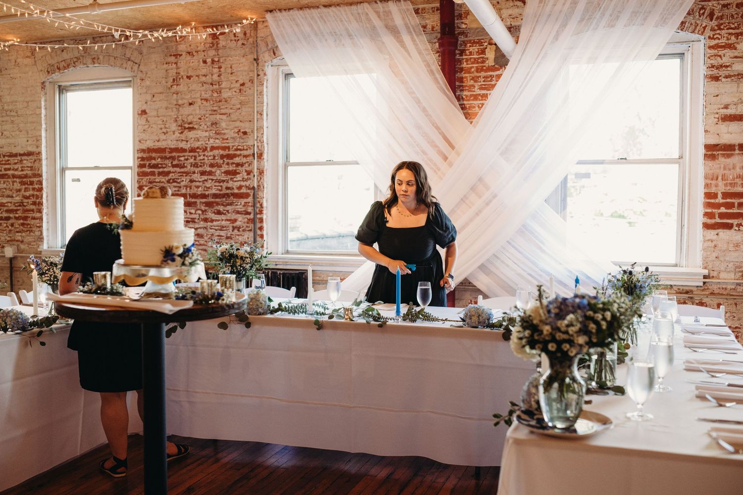 Wedding reception hall with white draping, exposed brick walls, and elegant table settings.