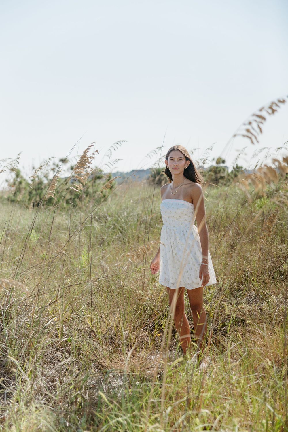 Person in white dress standing among tall grass in a sunny field.