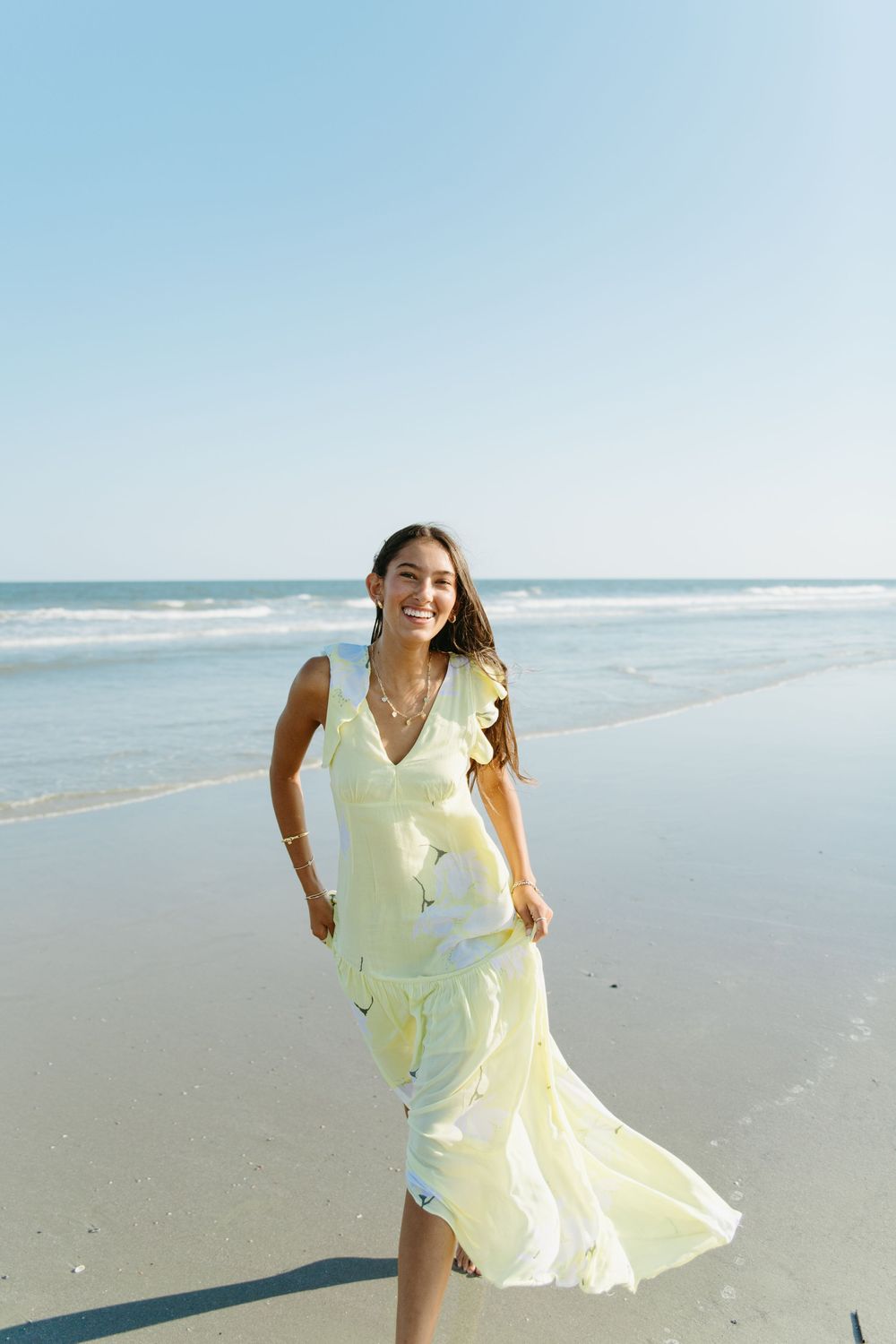 Yellow sundress twirling on empty beach with ocean waves in background.