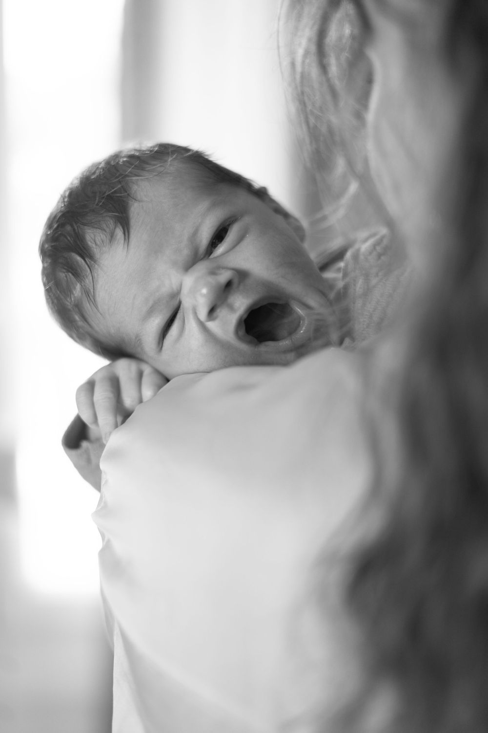 Black and white photo of a baby yawning while being held.