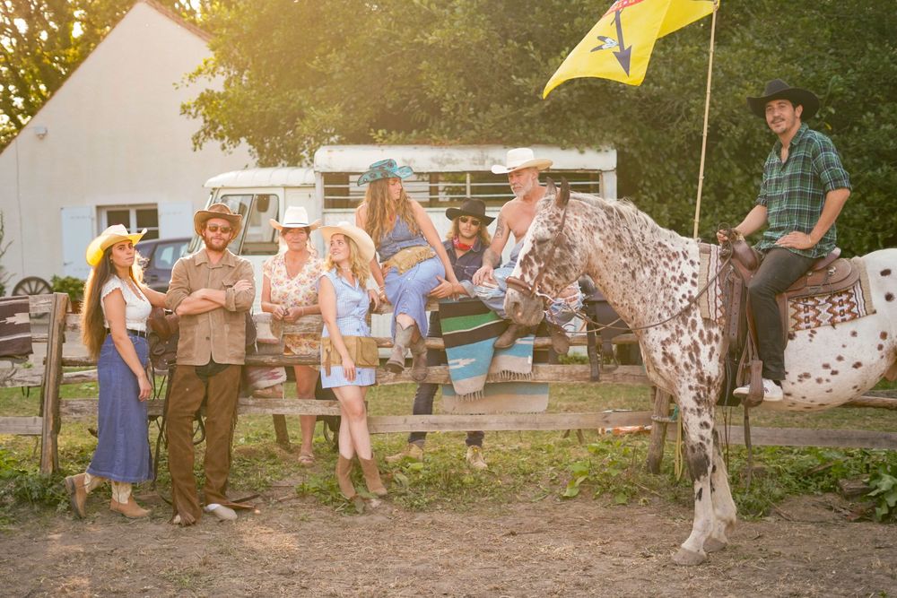 Group gathered around a spotted horse near a white building with a yellow flag.