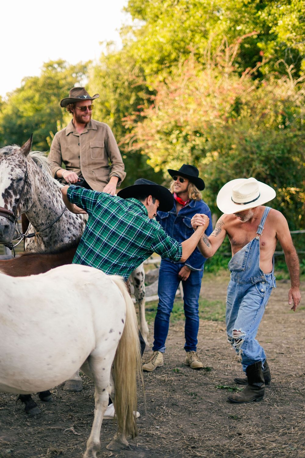 A group gathers around horses in a paddock, with one person adjusting a plaid blanket on horseback.
