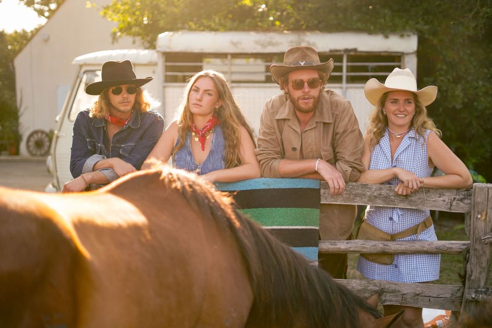 Group of friends leaning on a wooden fence near a horse at sunset.