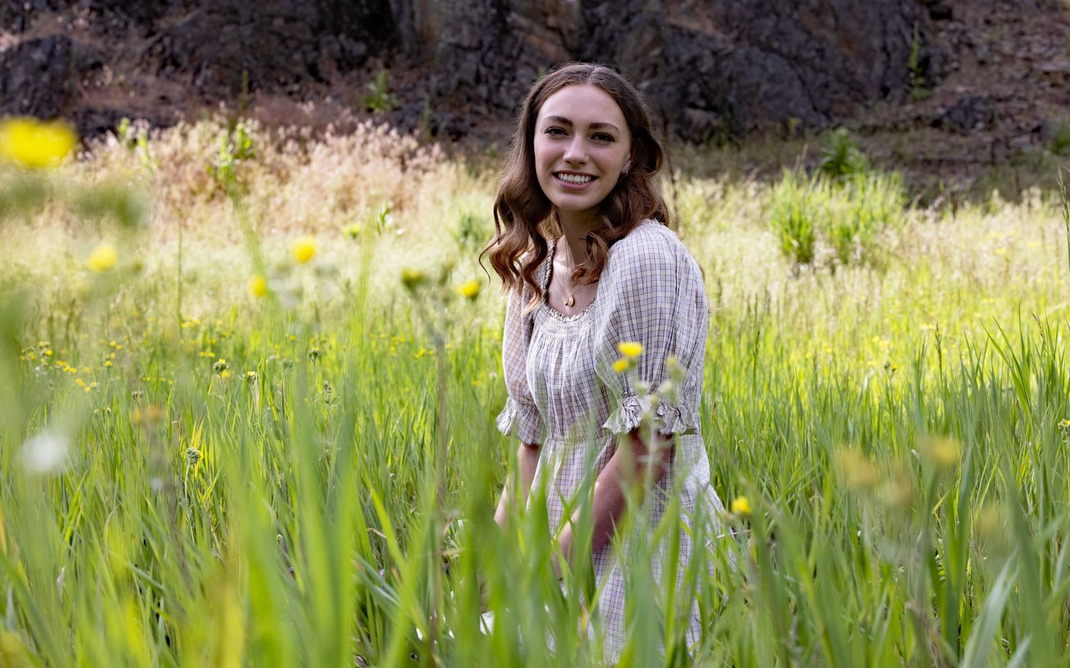 Person walking through tall grass in sunlit meadow wearing light colored dress.