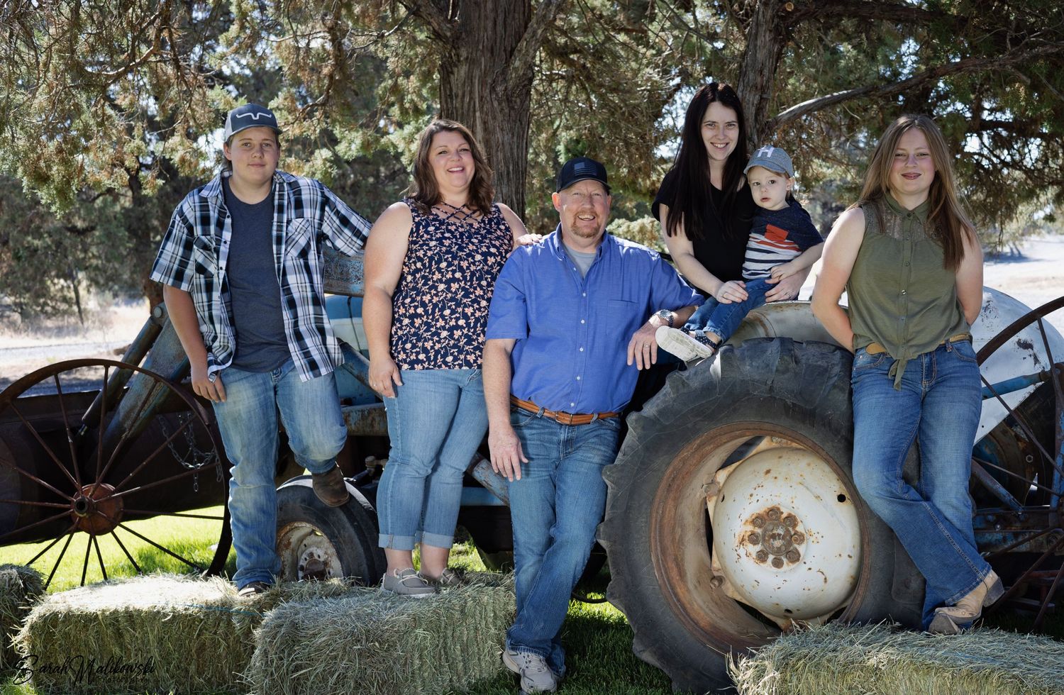 A group poses together by a large tractor wheel in a rustic outdoor setting.
