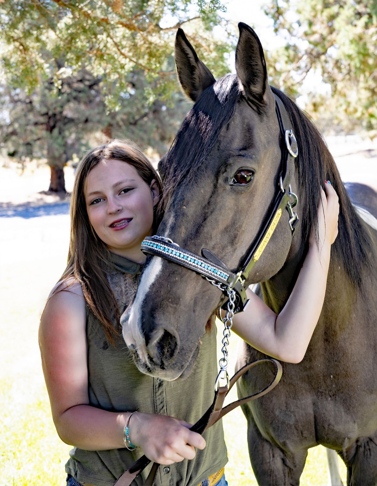 A close-up photo of someone posing with a dark brown horse wearing a halter.