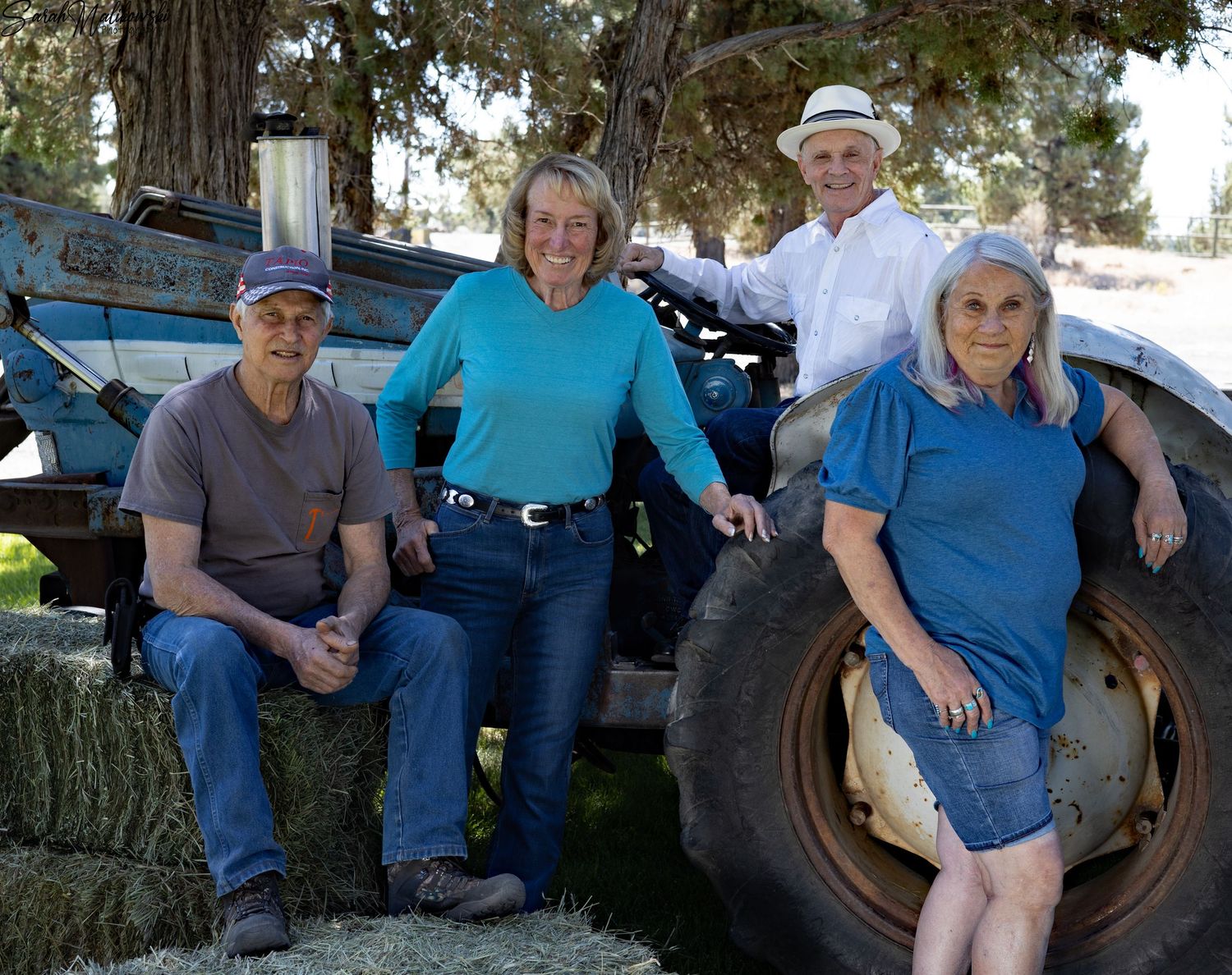 A casual group poses together near a large tractor tire in an outdoor rural setting.