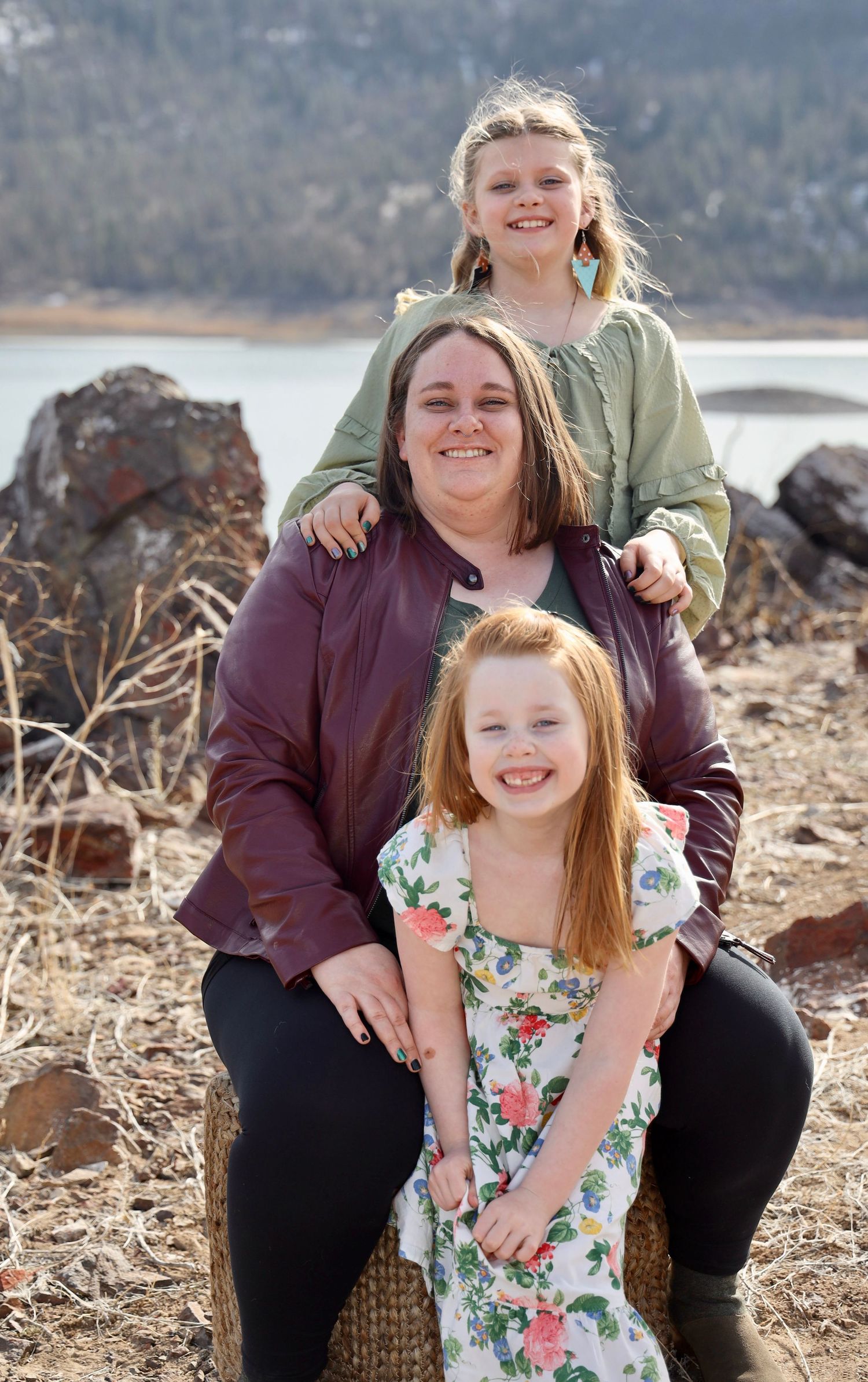 Family portraits on rocky terrain near water with floral dress and casual wear.