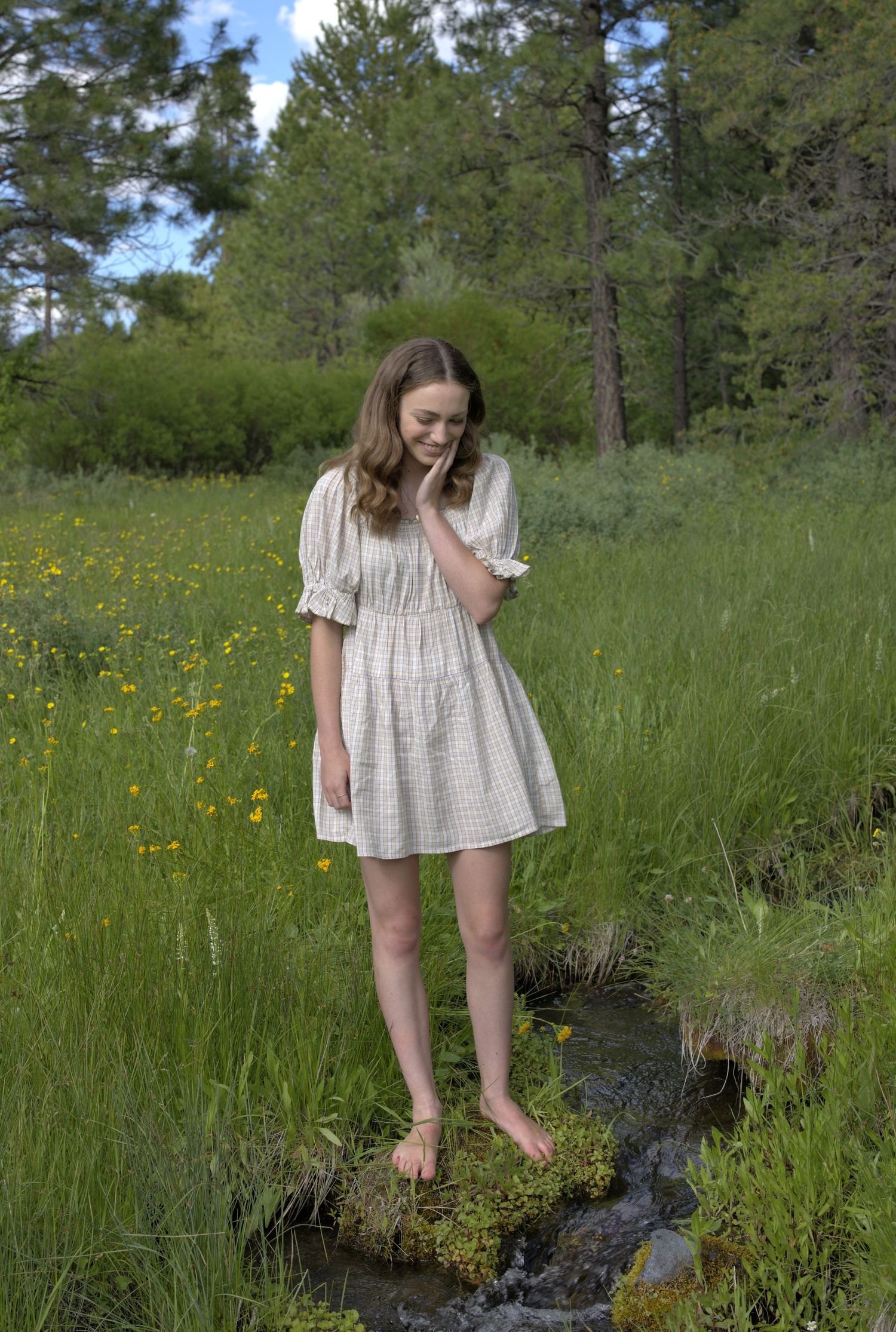 Figure in white dress exploring meadow with wildflowers and tall grass on sunny afternoon.