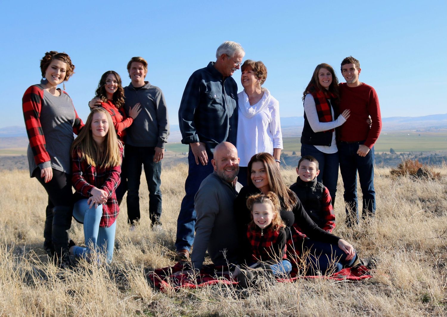 A large family group poses together on a hillside with mountains in the background.