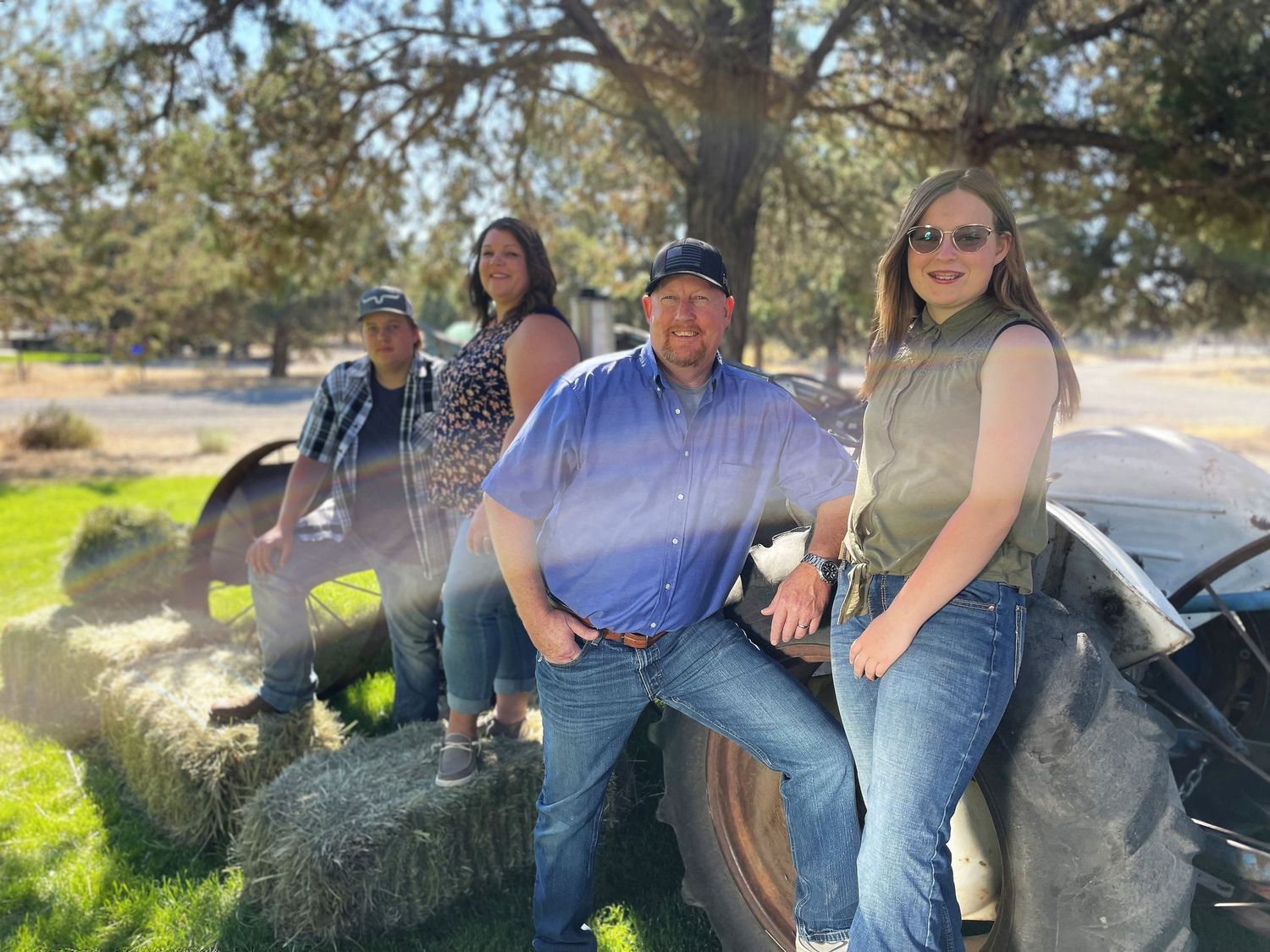 A group sits casually on large tractor tires in a sunny outdoor setting.