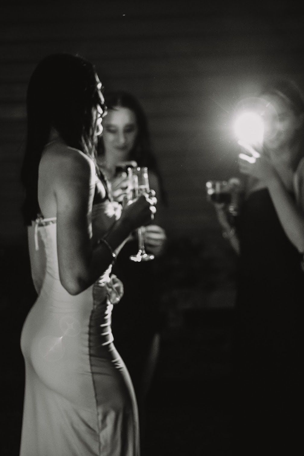 Black and white photo of person take flash photo at night of model facing away from camera in a white long dress