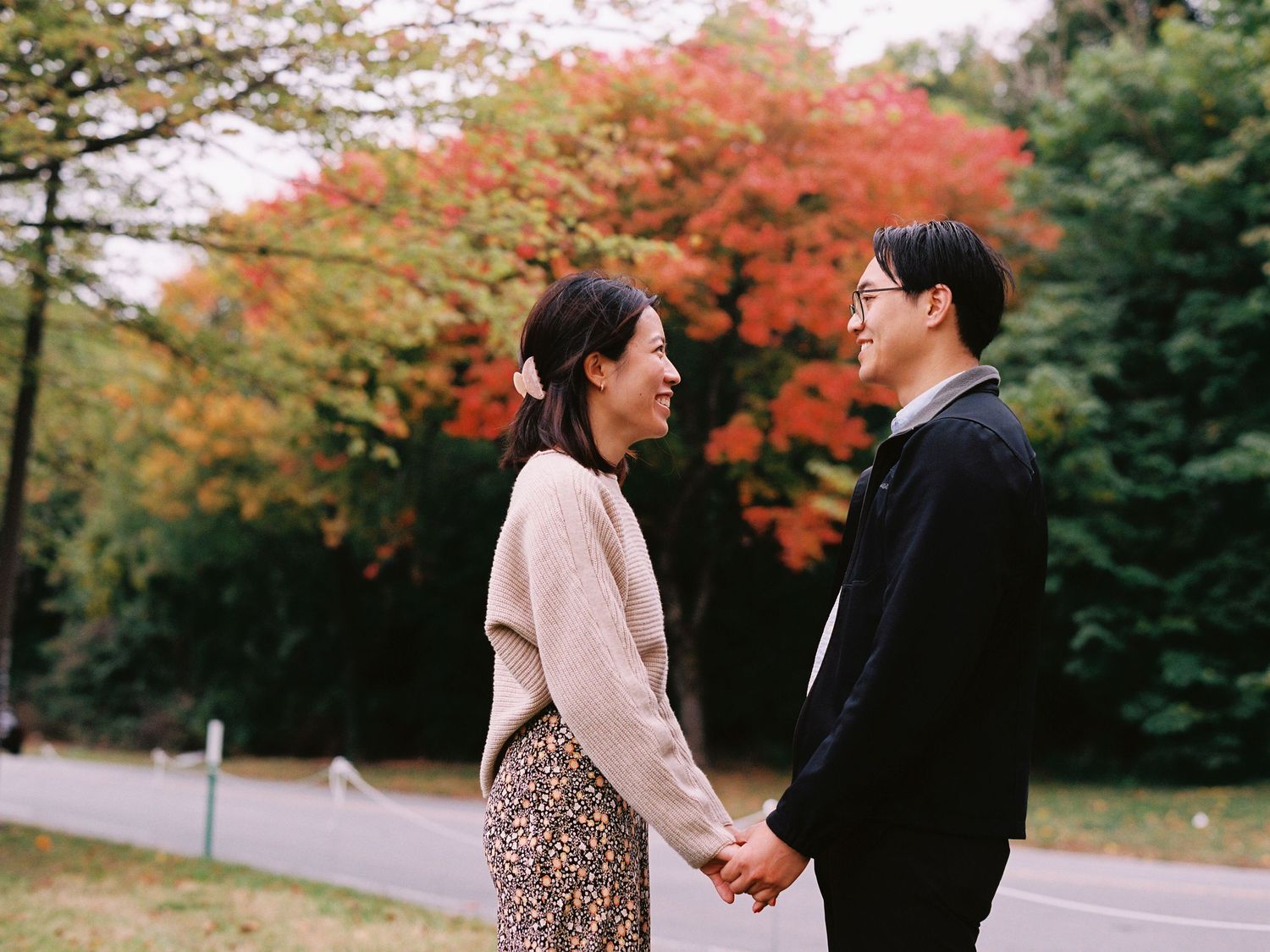 Romantic couple holding hands in front of vibrant fall foliage on a scenic path.