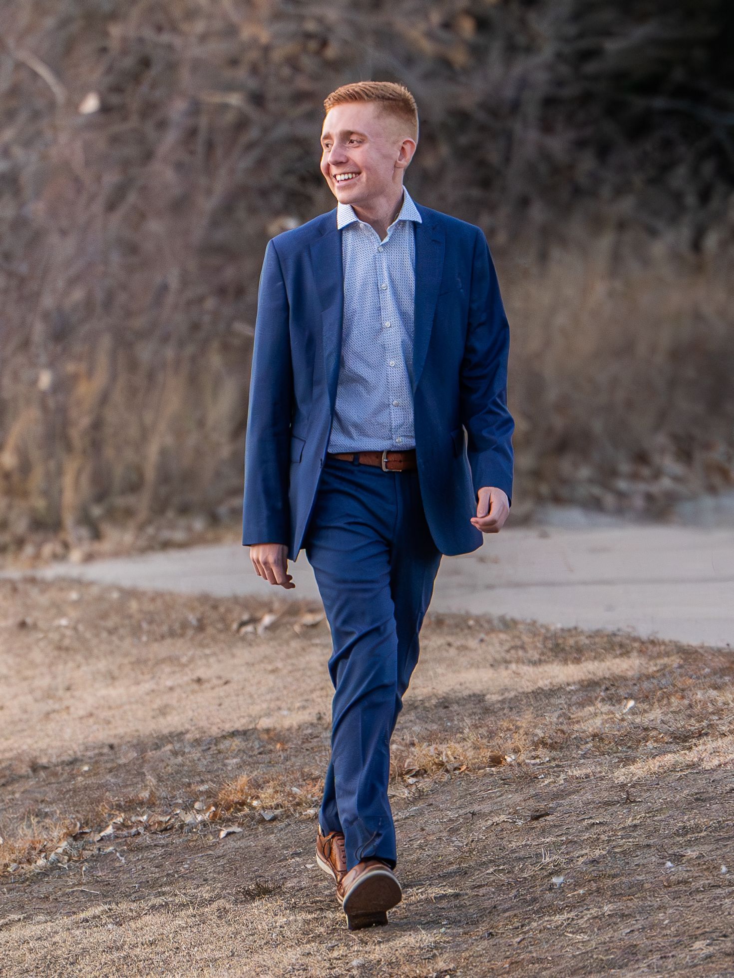 A person in a navy suit walks along a dirt path during autumn.