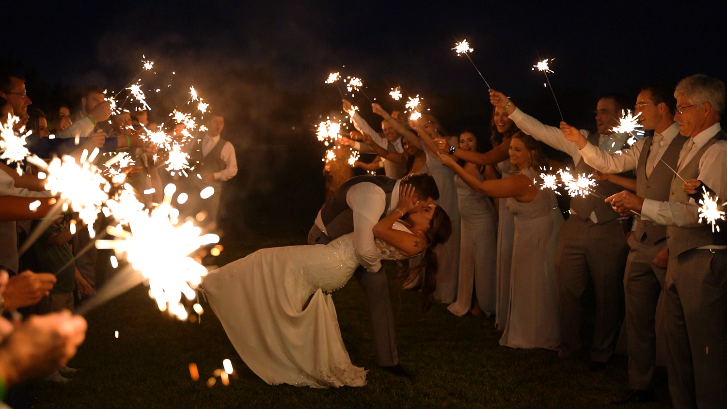 Wedding couple shares a romantic dip under sparkler exit arch.