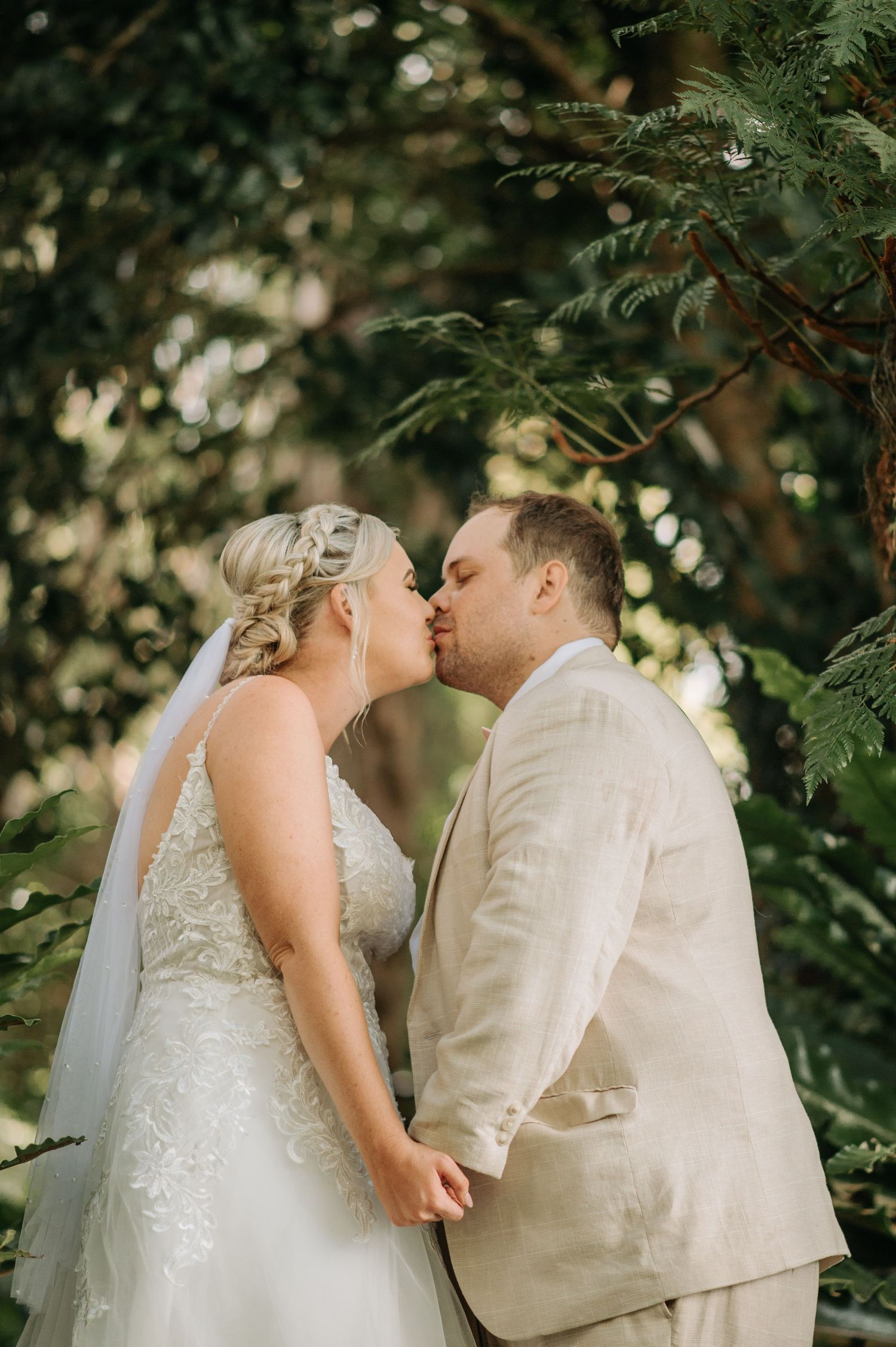 Romantic wedding couple shares an intimate kiss surrounded by green foliage.
