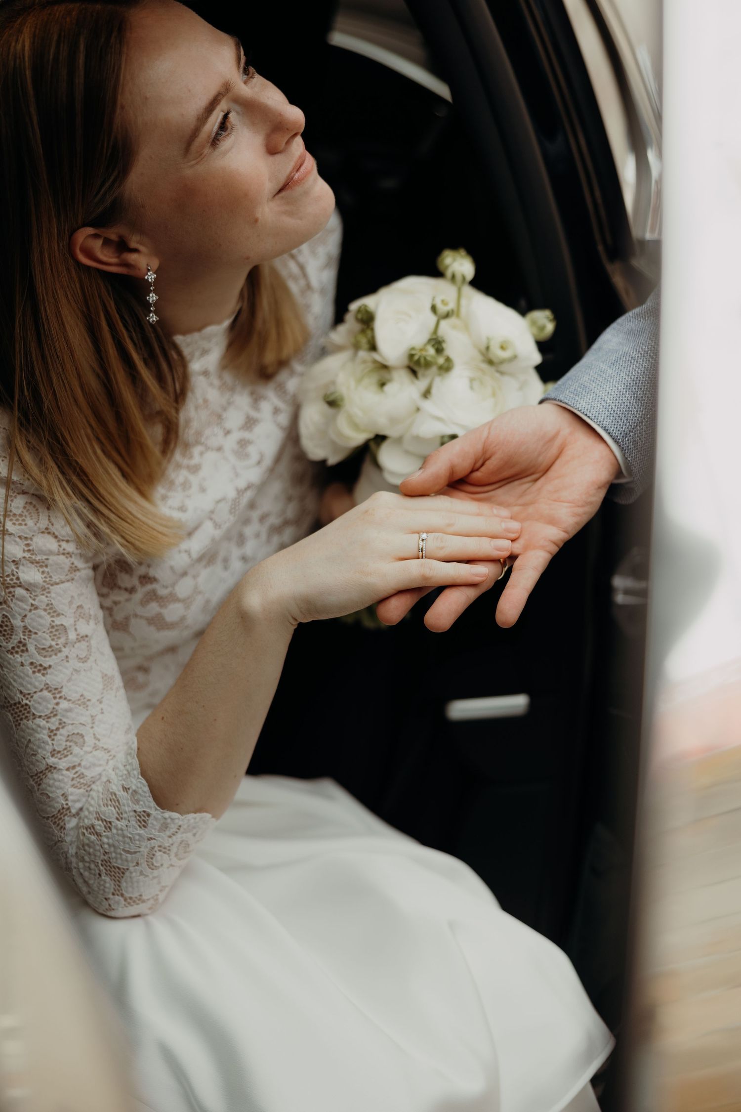 Close-up of a lace-clad bride showing her wedding ring with white roses in hand.