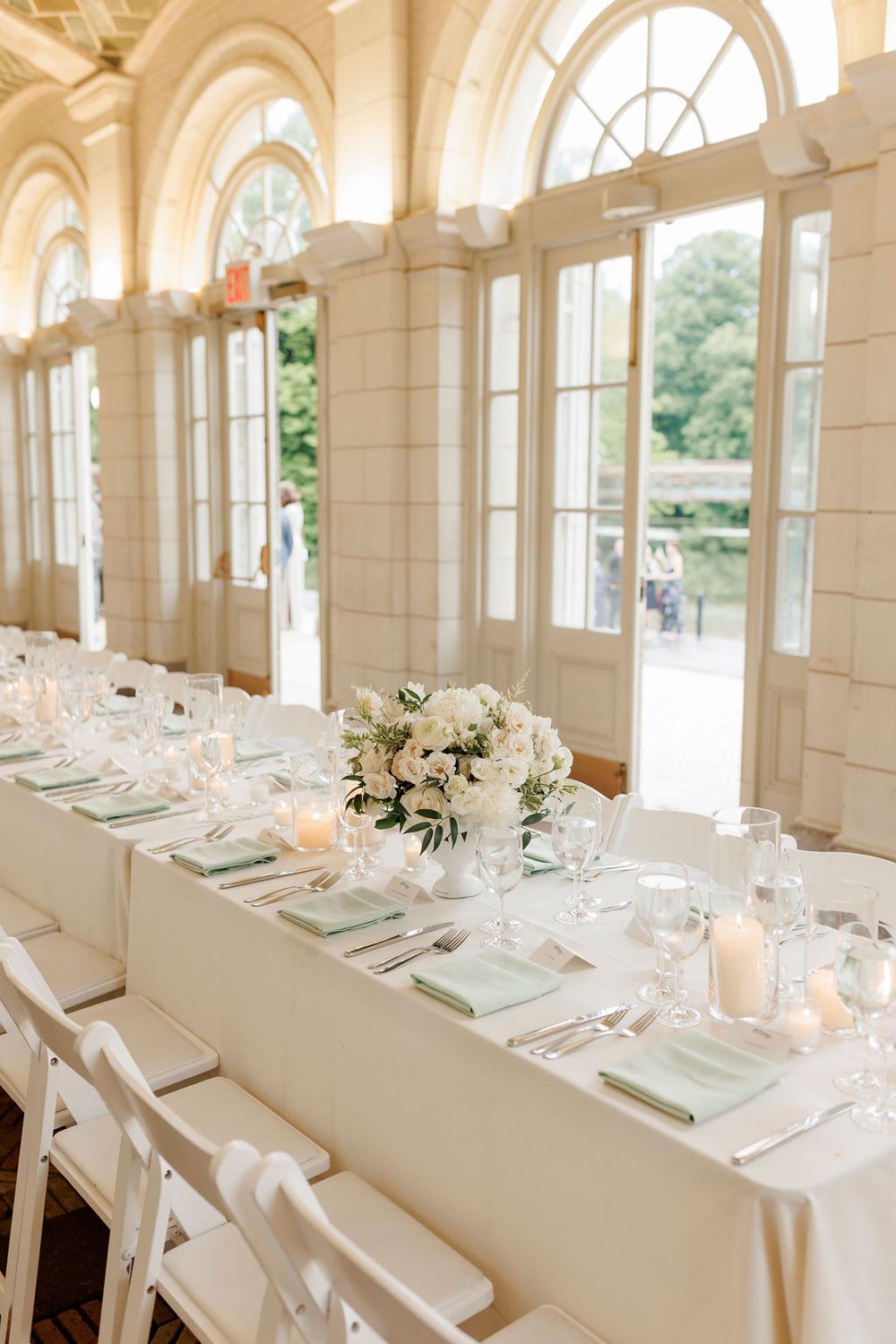 An elegant wedding reception table setting with white florals and place settings in a sunlit venue.