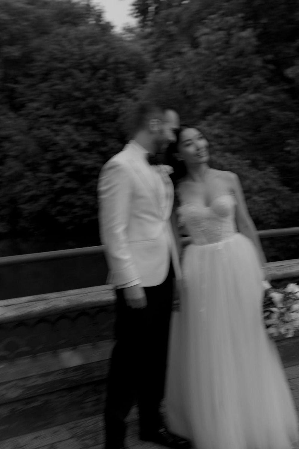 Romantic black and white photo of couple embracing on bridge.