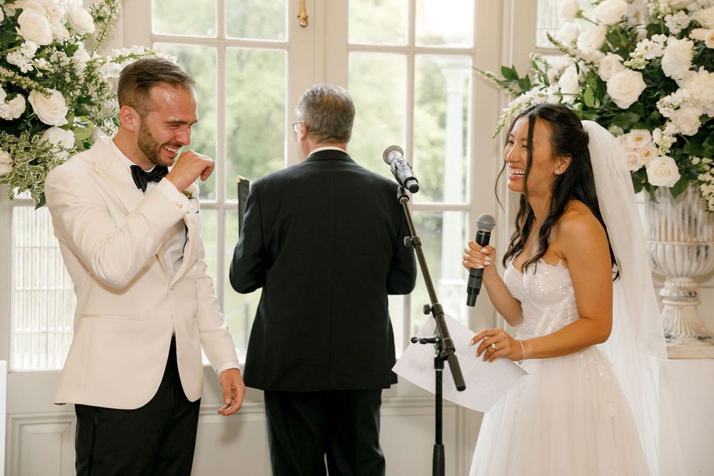Wedding ceremony moment in a bright sunlit room with elegant white floral arrangements.