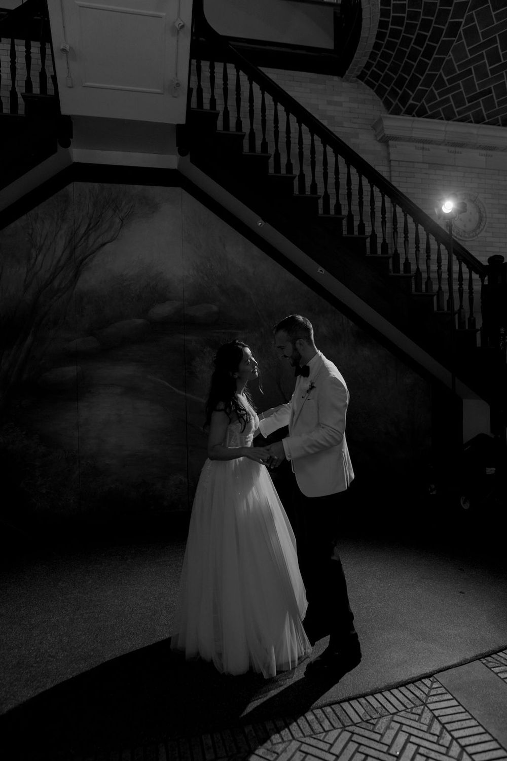 A romantic black and white dance moment between newlyweds under dramatic lighting.