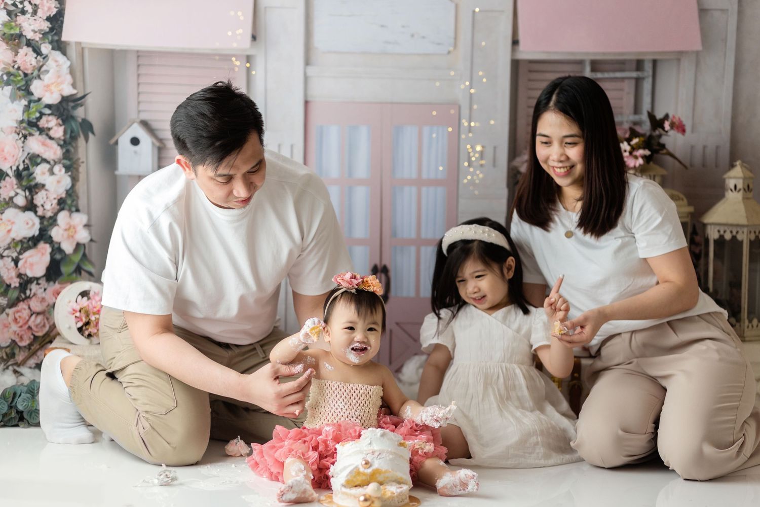 Family gathered on floor with pink floral decorations and cakes for celebration.