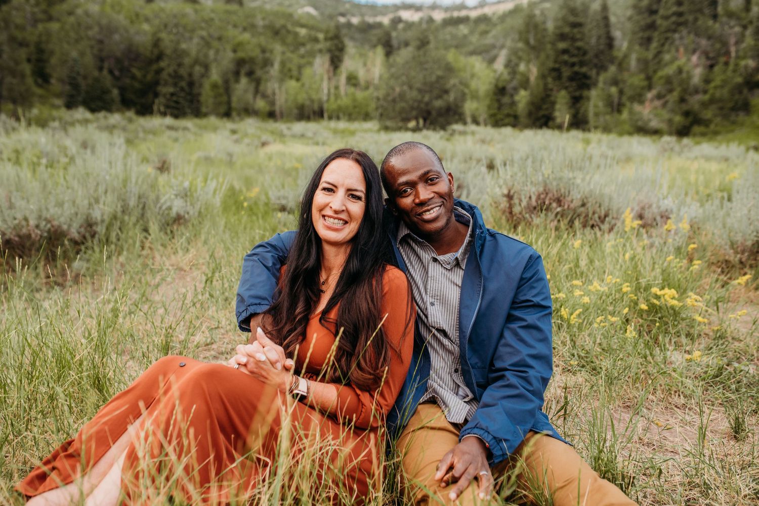 Couple sitting together in a scenic mountain meadow filled with wildflowers and natural beauty.