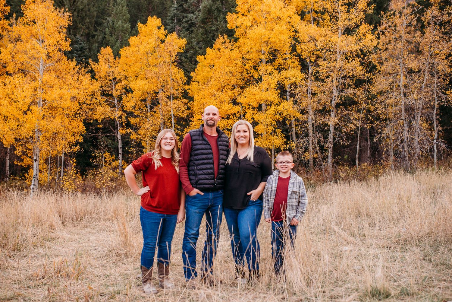 Small family group posed together in field with golden aspen trees behind them.