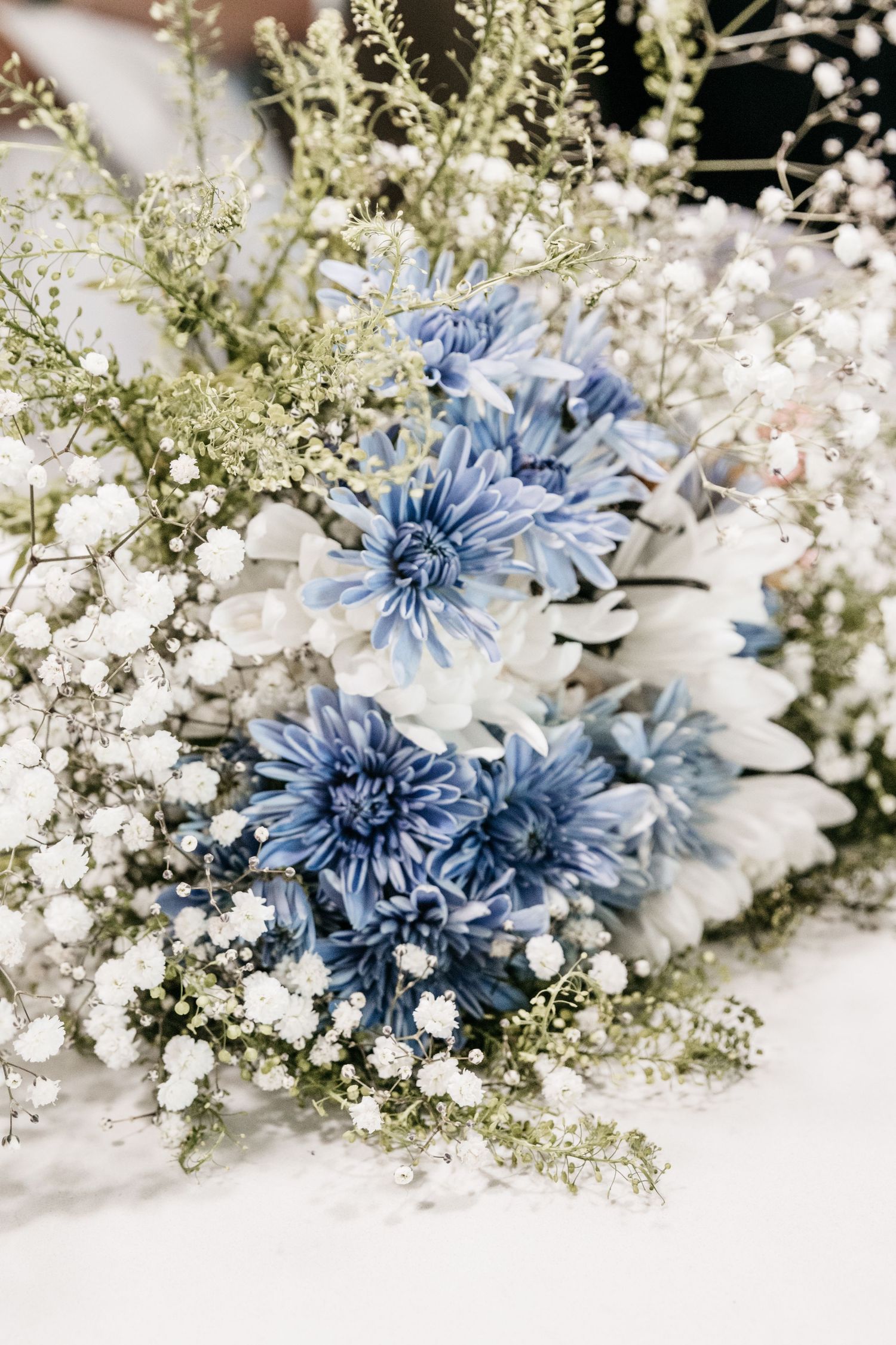 Delicate floral arrangement featuring blue chrysanthemums and white baby's breath.