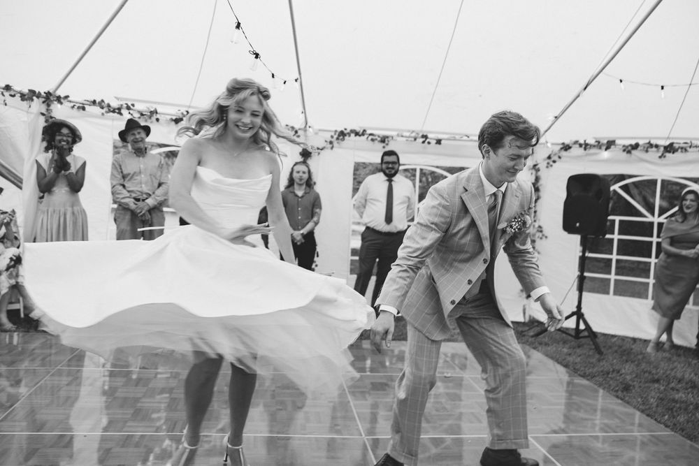 Bride and groom share joyful first dance under a marquee tent at an outdoor wedding reception.